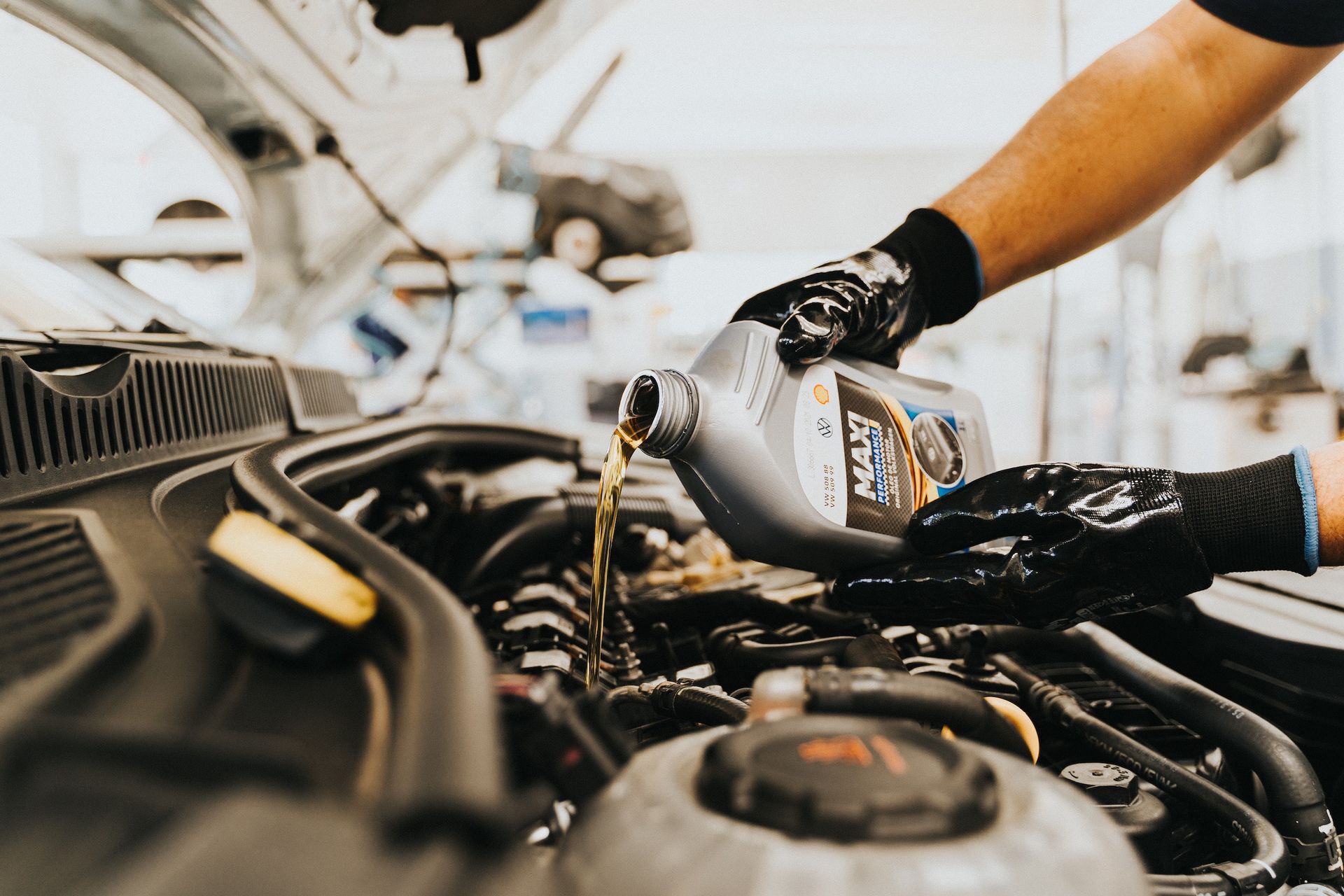 Person in gloves pouring oil into a car engine during an oil change.