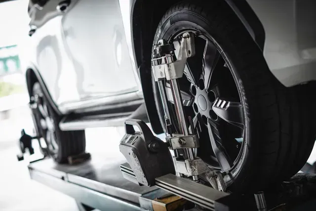 A white car on a lift; wheel alignment equipment attached to front tire.