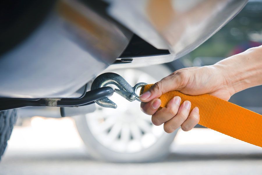 Hand attaching an orange tow strap hook to a vehicle's frame.