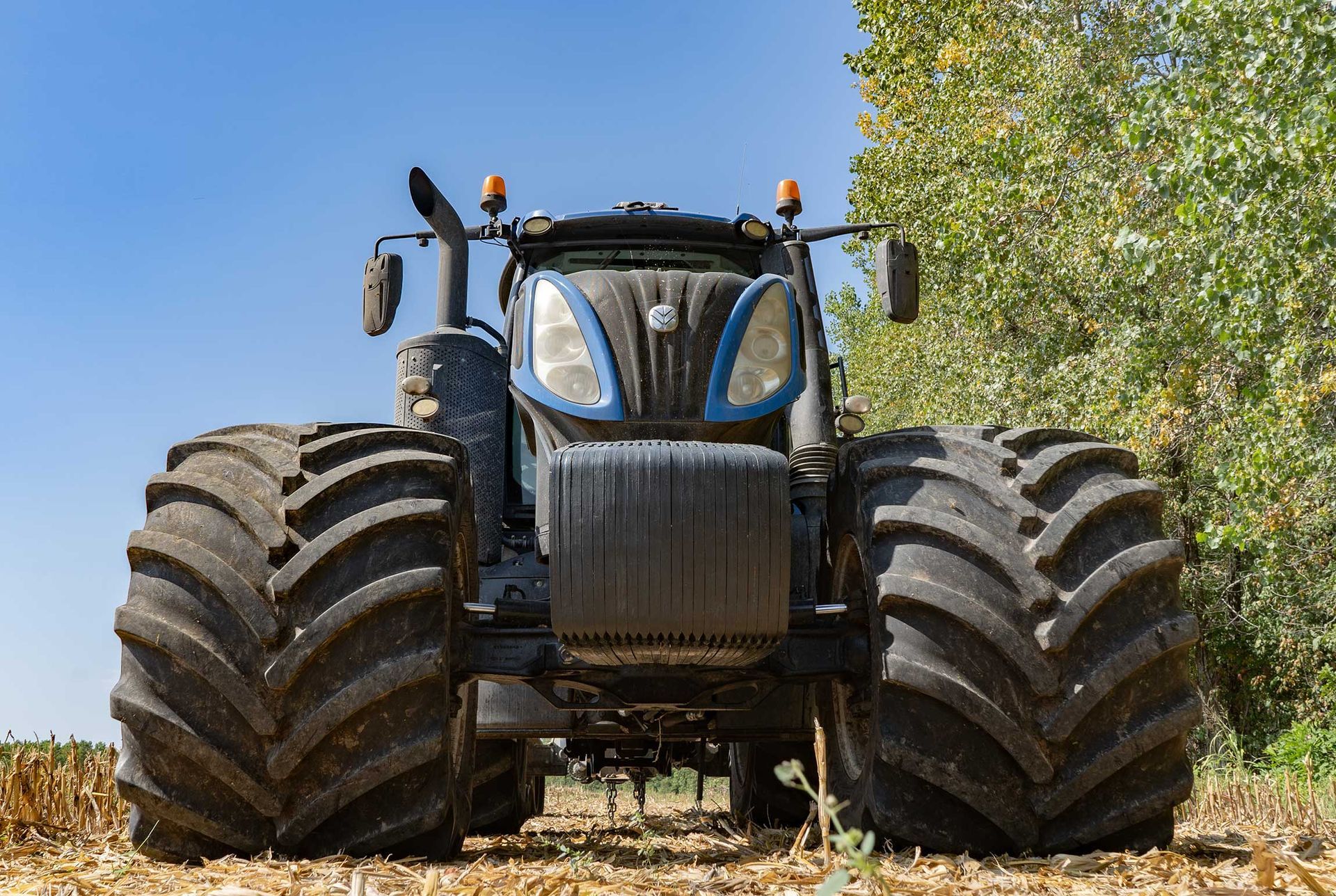 Blue and black tractor with large tires in a field under a blue sky.