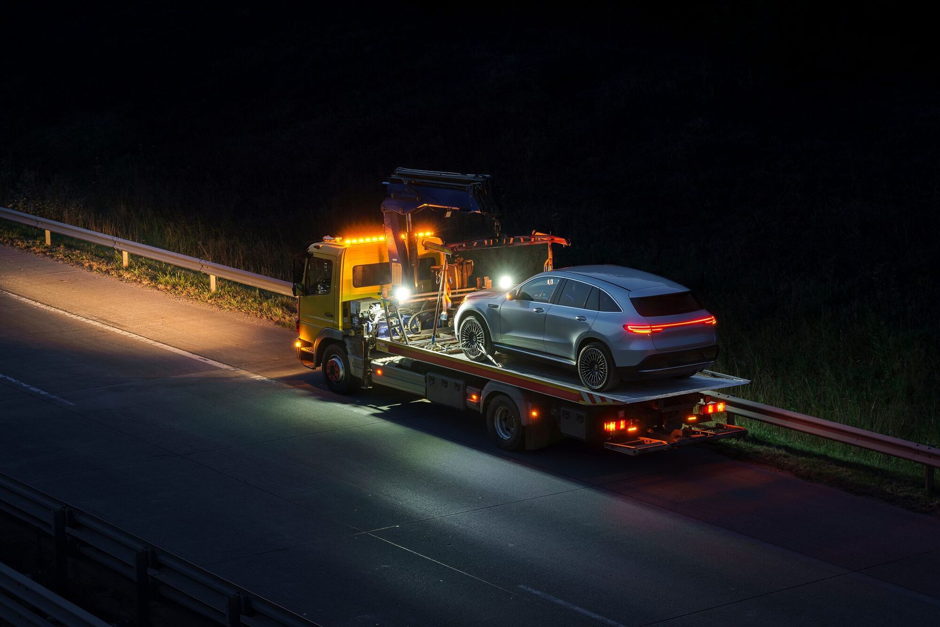 Tow truck with car loaded at night on a dark highway.