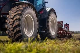 A tractor plowing a field, close-up of large tires on grass, blue sky.