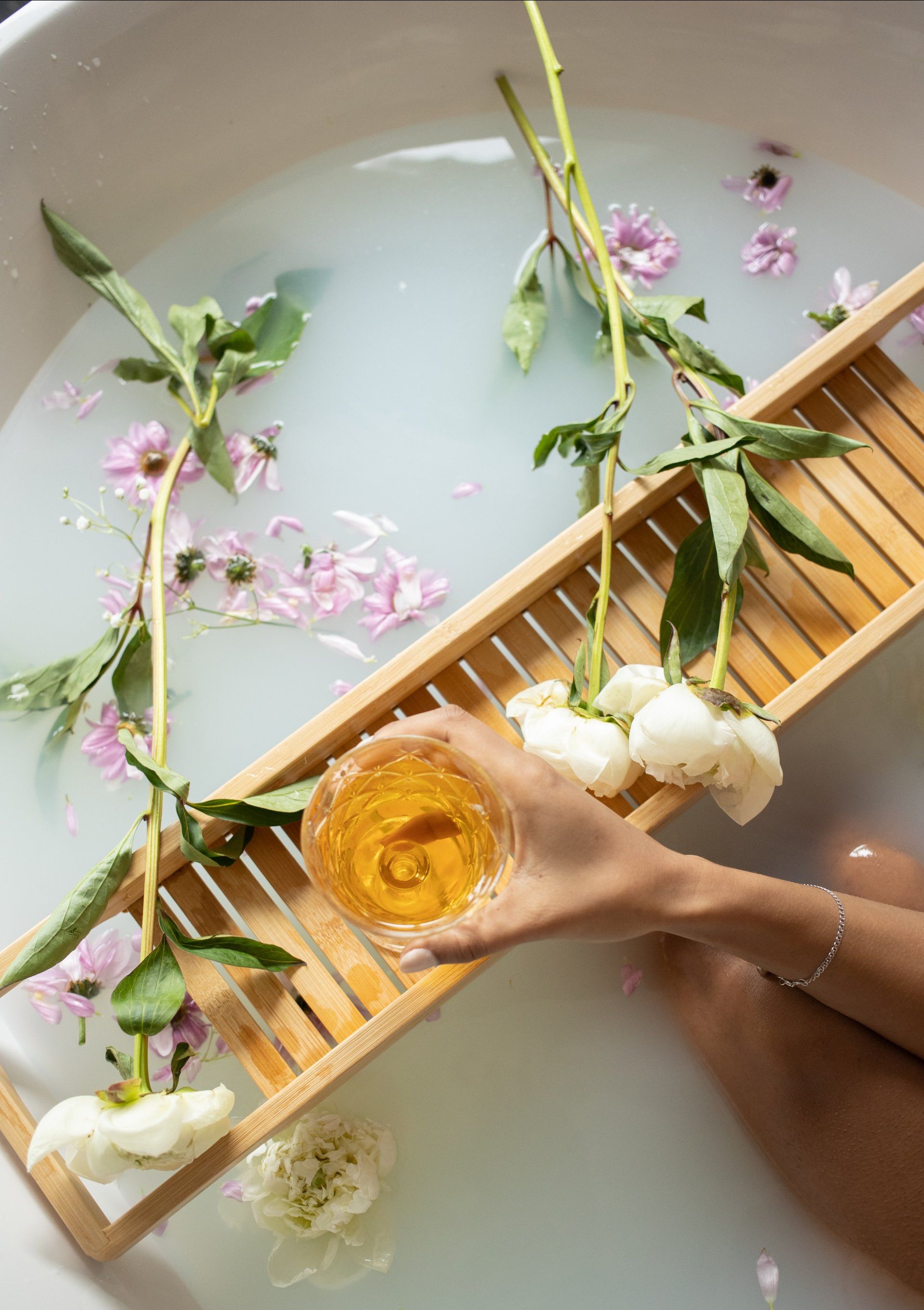 A woman is taking a bath with flowers and a glass of wine.