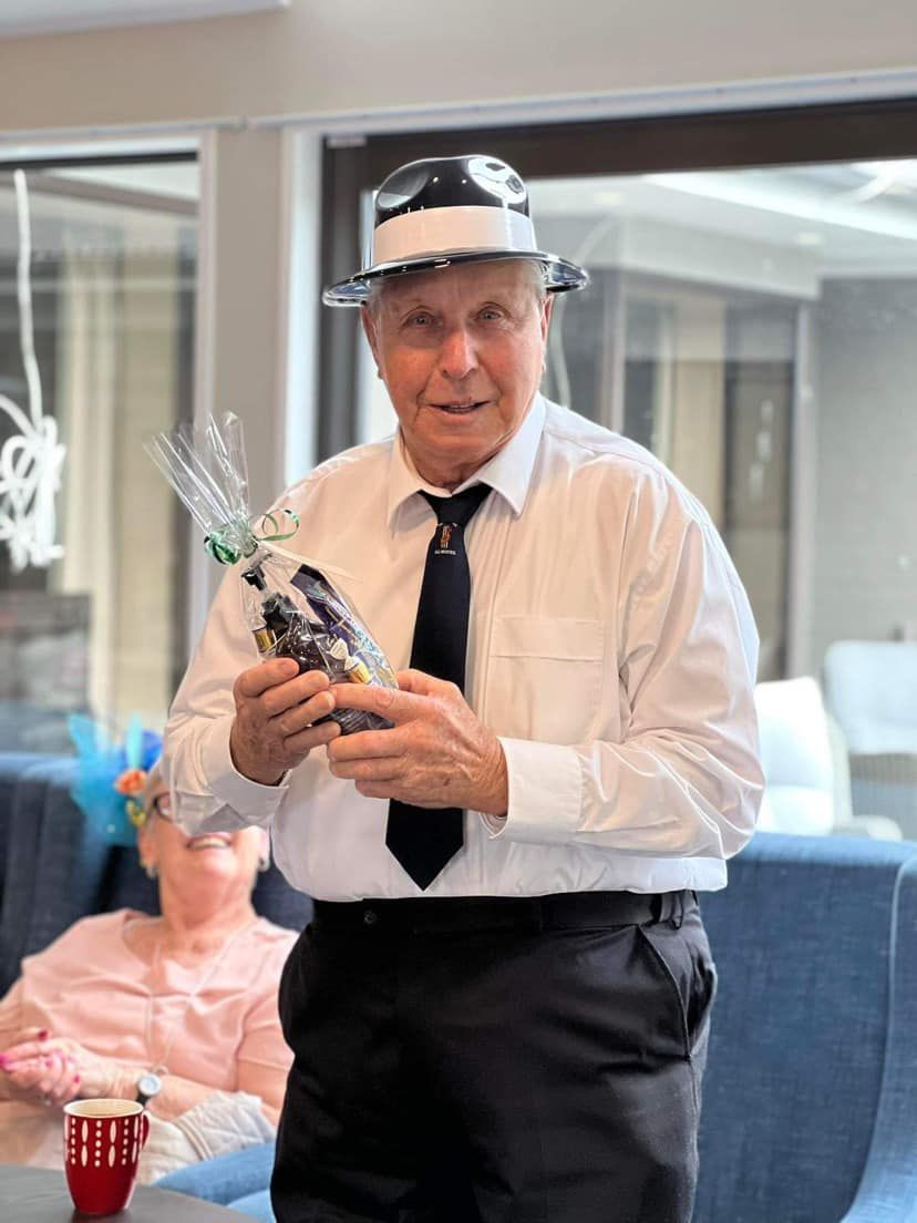 A man wearing a hat and tie is holding a bouquet of flowers.