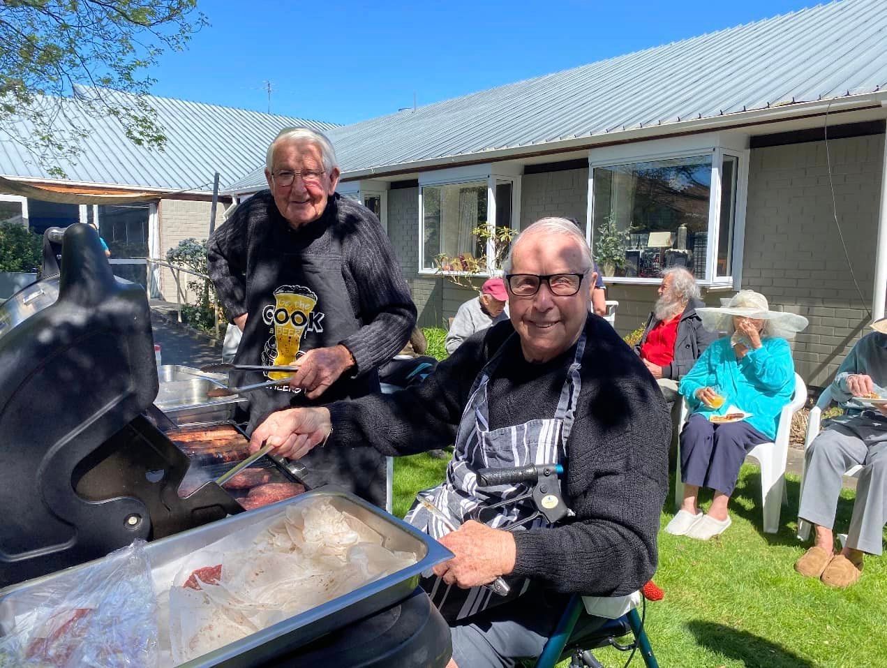 A group of elderly people are sitting around a grill.
