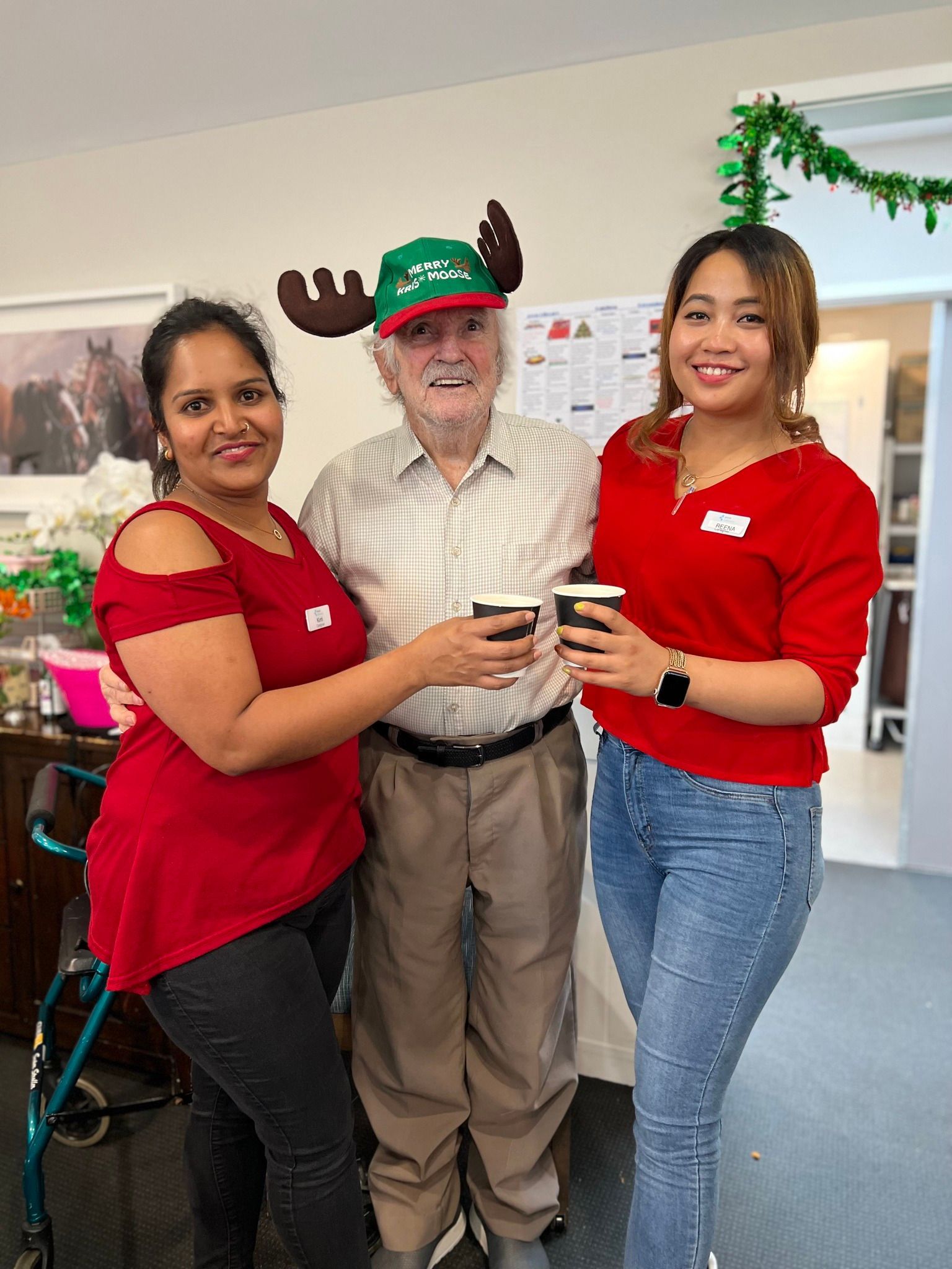 A man wearing a reindeer hat is standing next to two women.