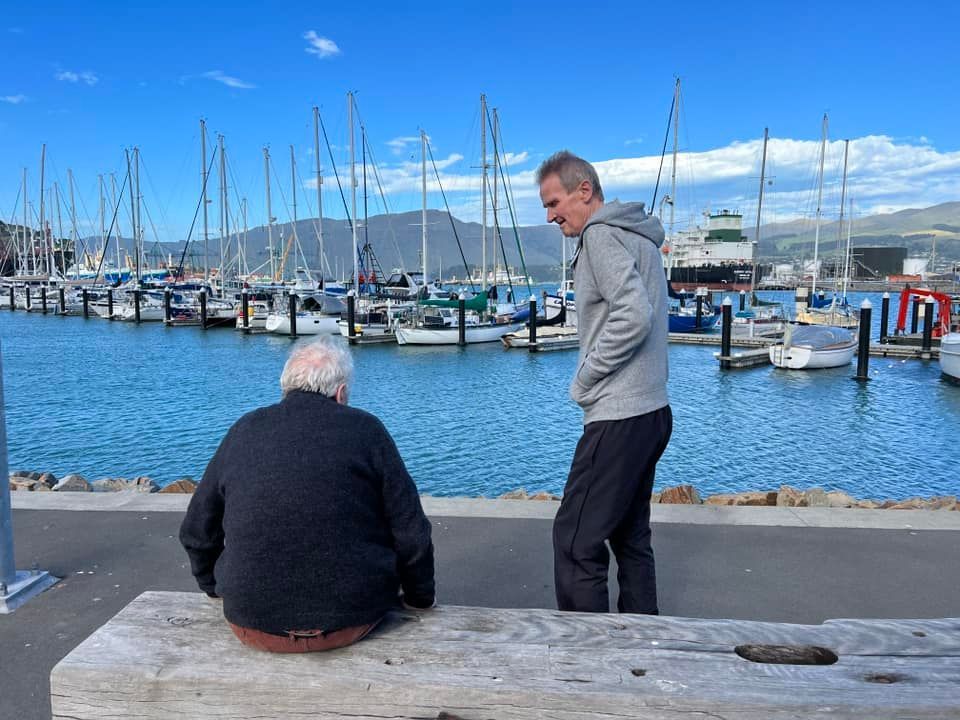 Two men are sitting on a bench in front of a marina
