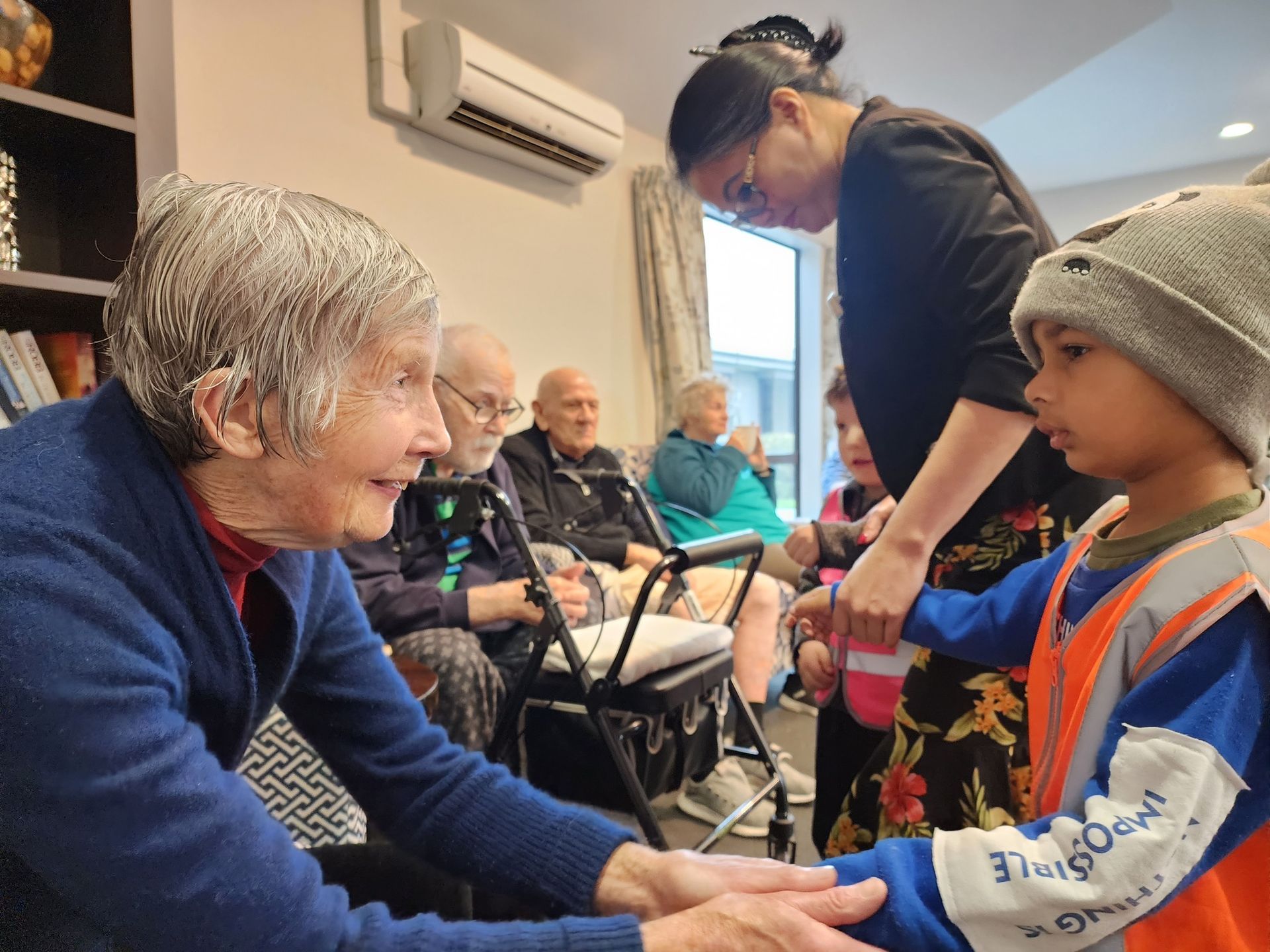 An elderly woman is holding the hand of a young boy in a living room.