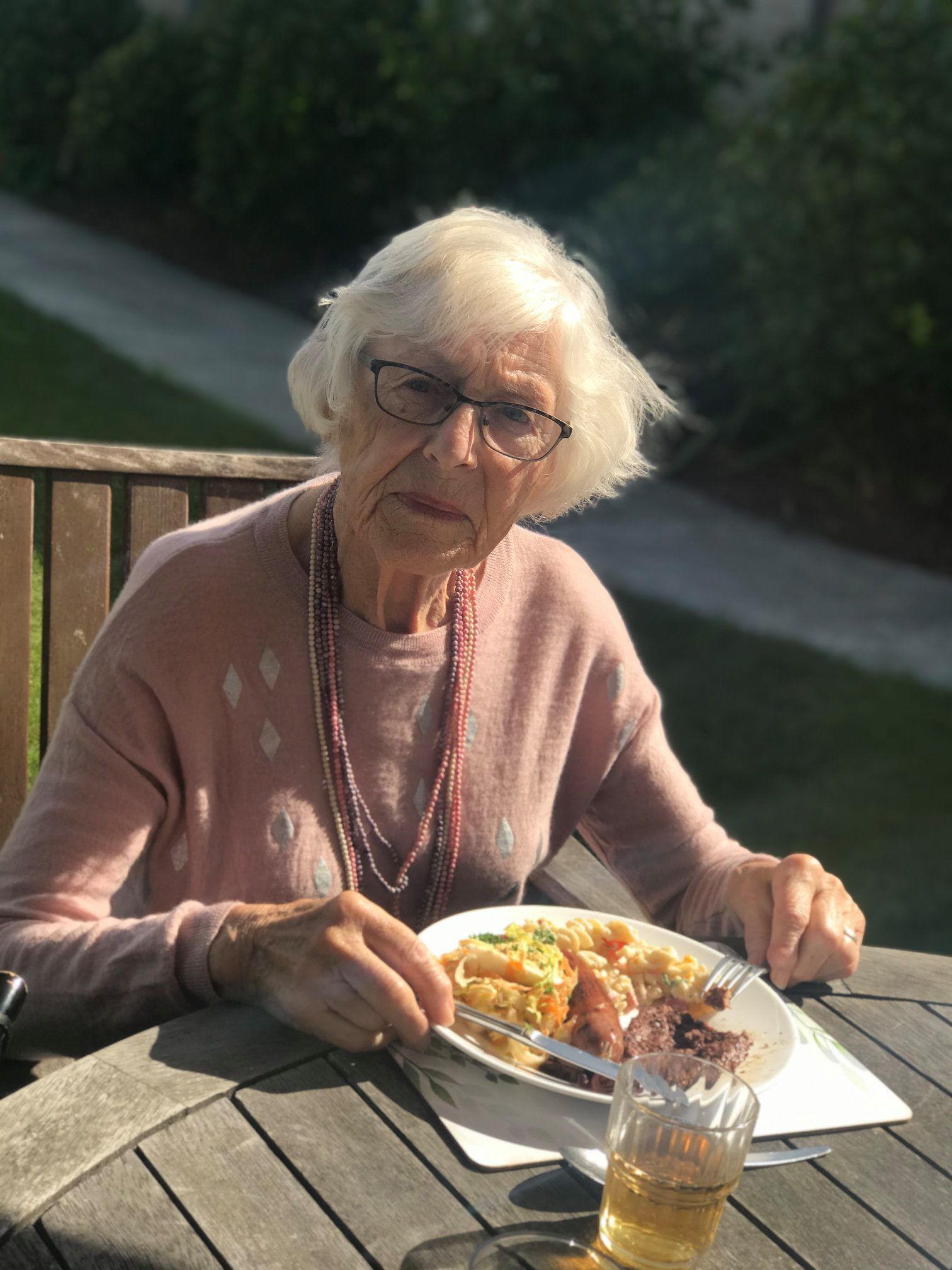 An elderly woman is sitting at a table eating a plate of food.