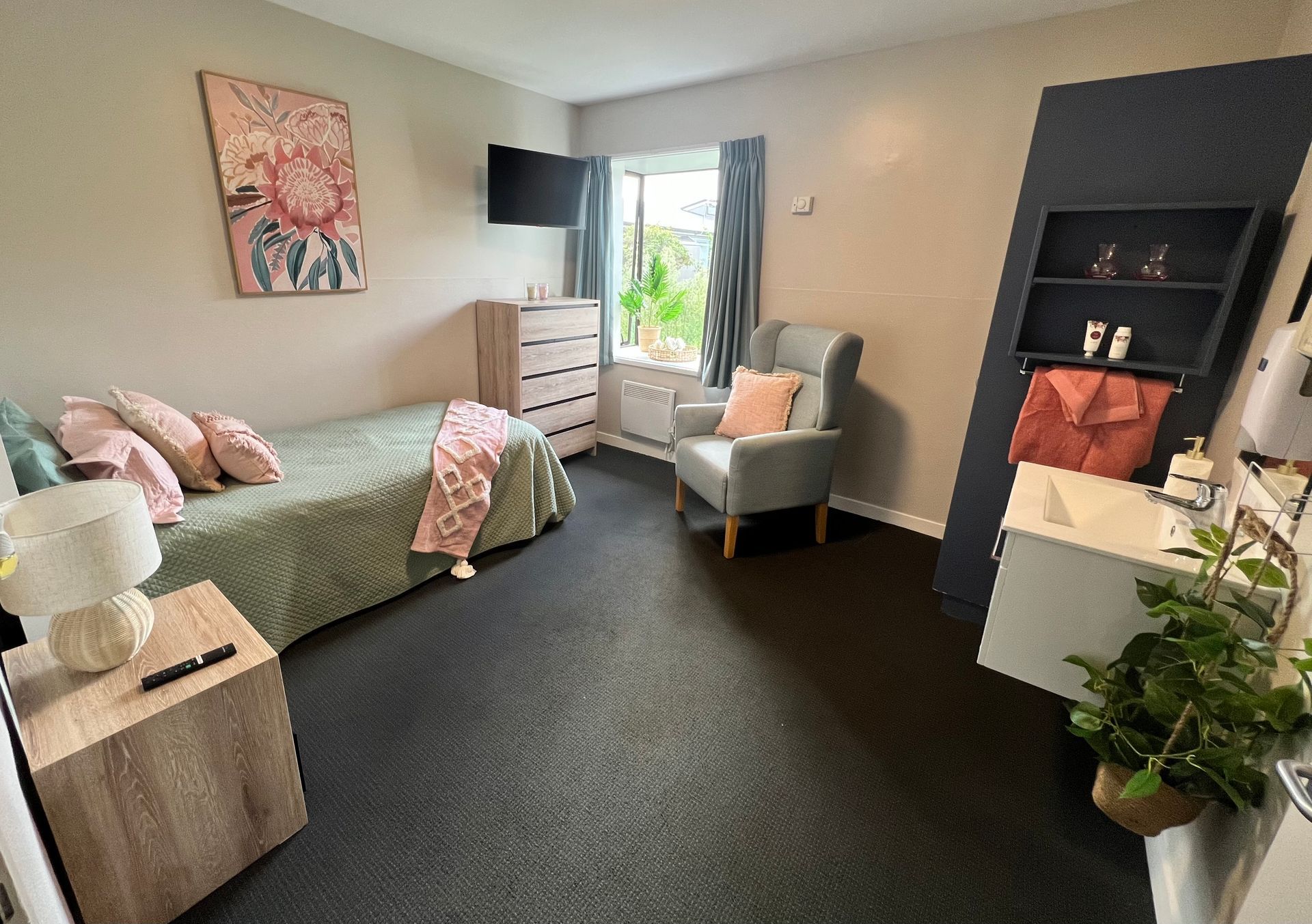 A bedroom with a single bed , chair , nightstand and dresser.