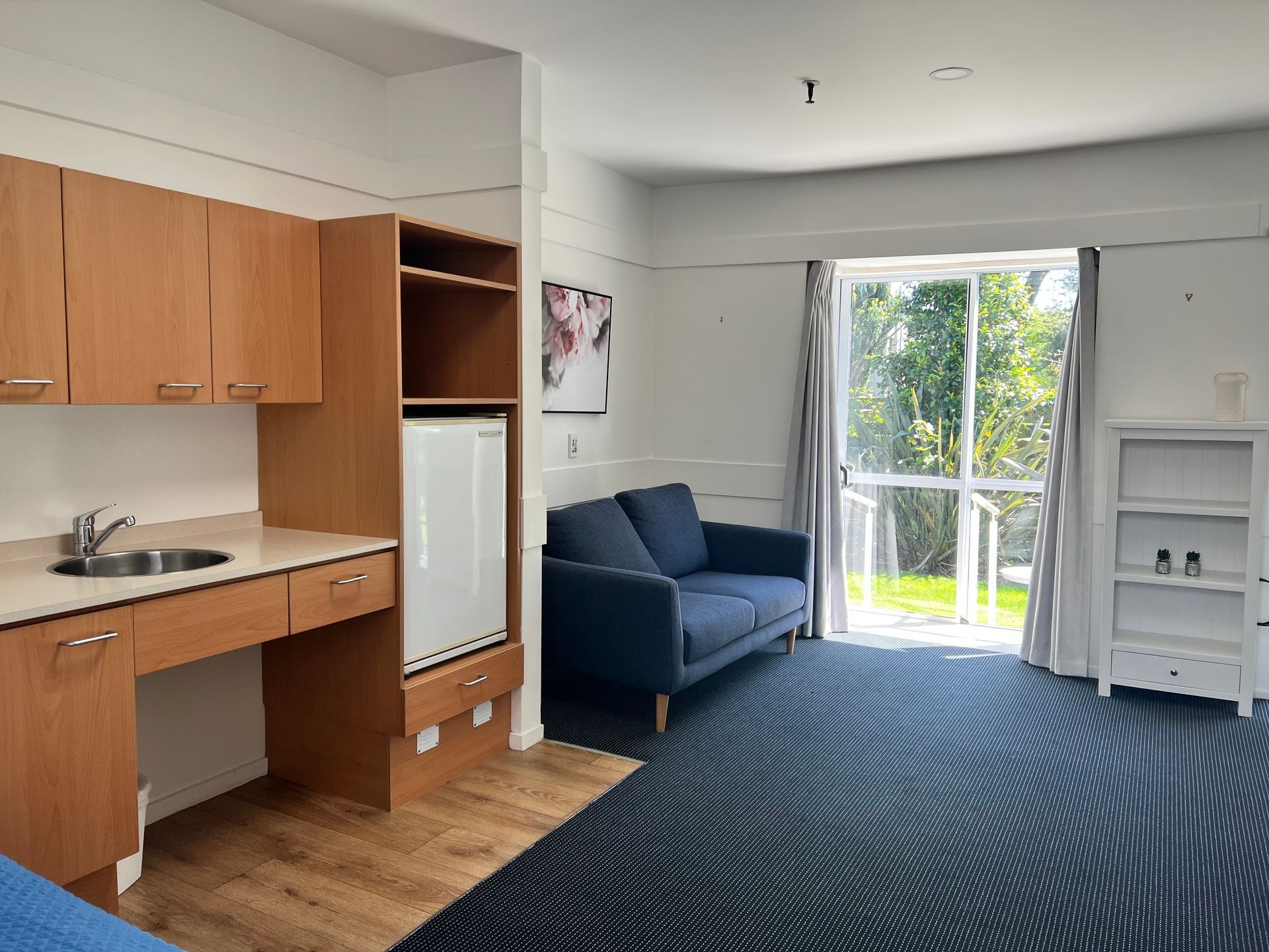 A living room with a blue couch , a sink , and a sliding glass door.