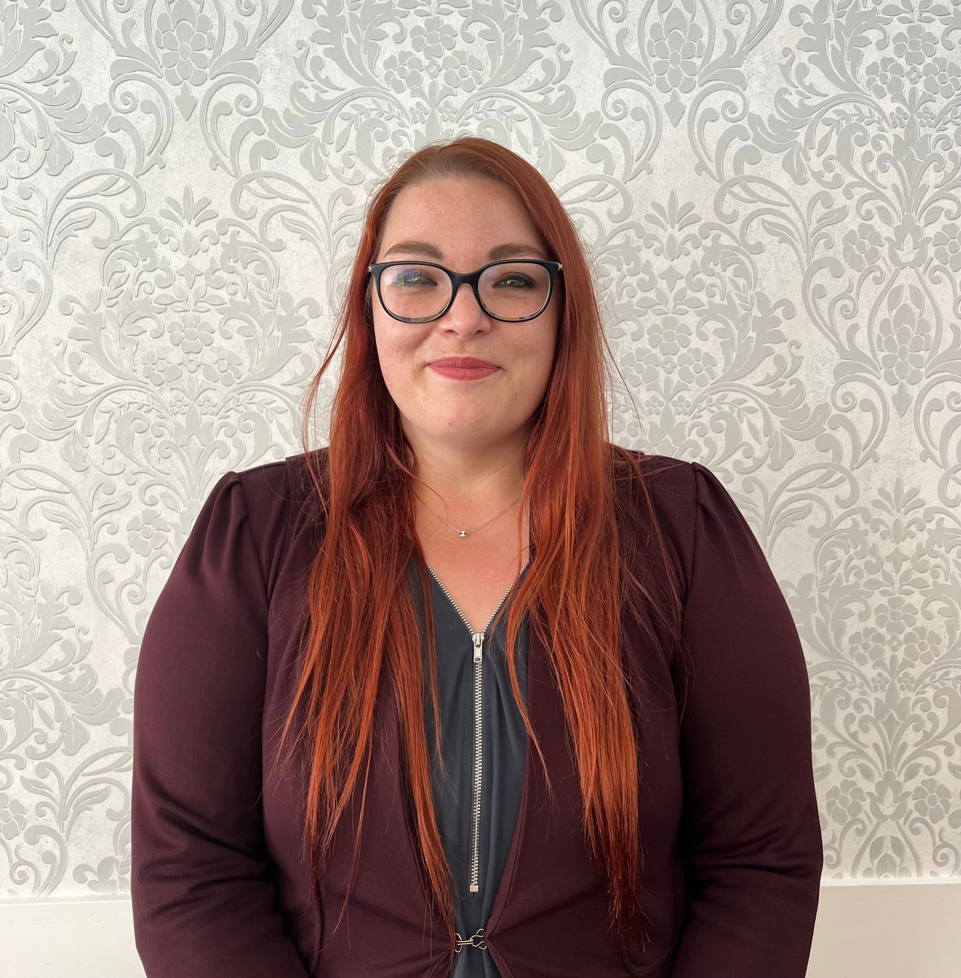a woman with red hair wearing glasses and a maroon jacket