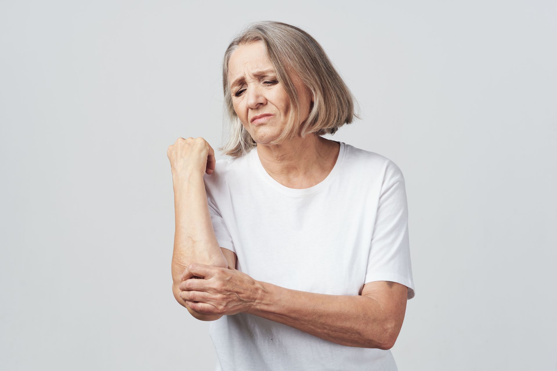 Uma mulher idosa está segurando o cotovelo com dor.