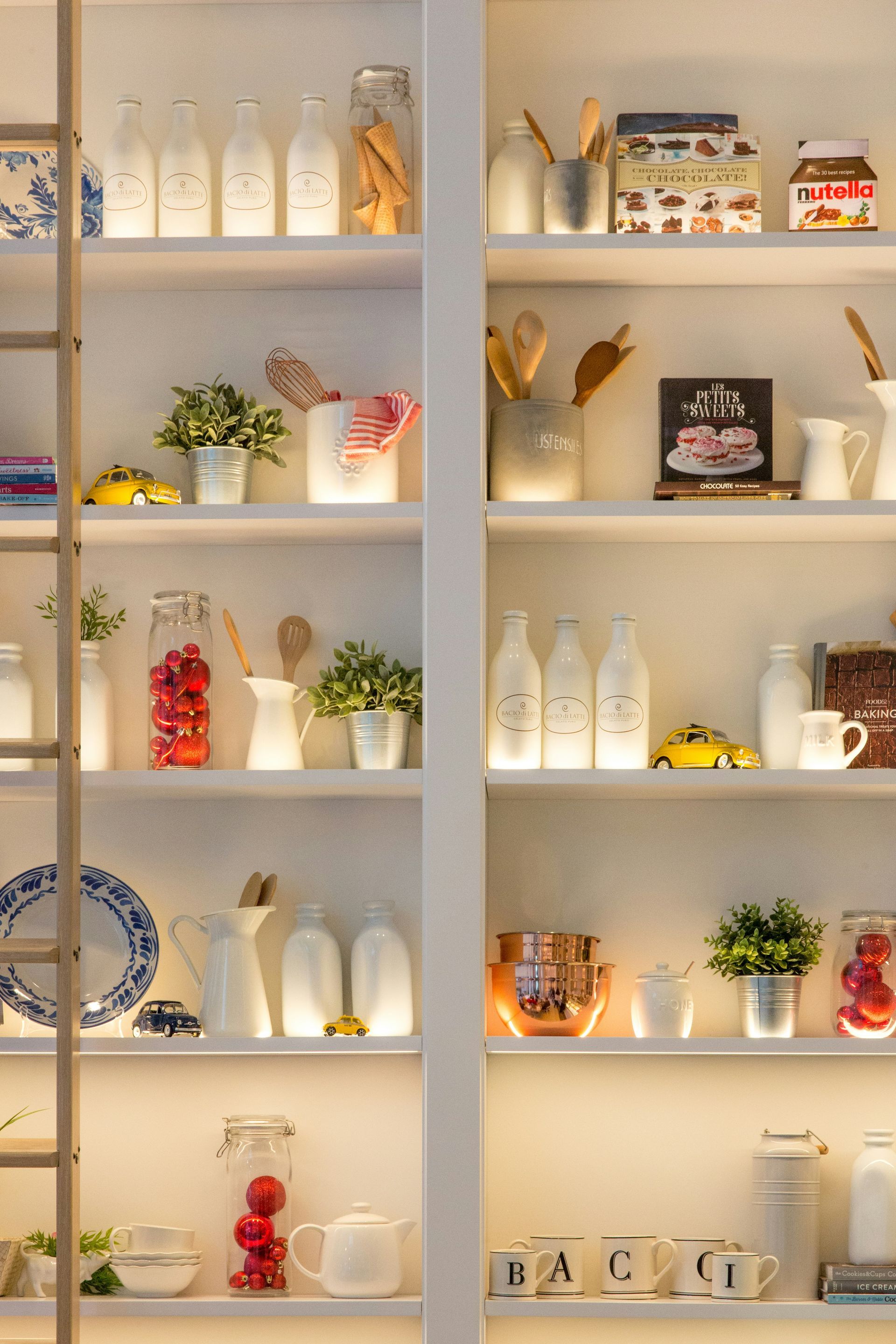 White shelving unit with illuminated shelves, displaying bottles, plants, kitchenware, and decorative items.