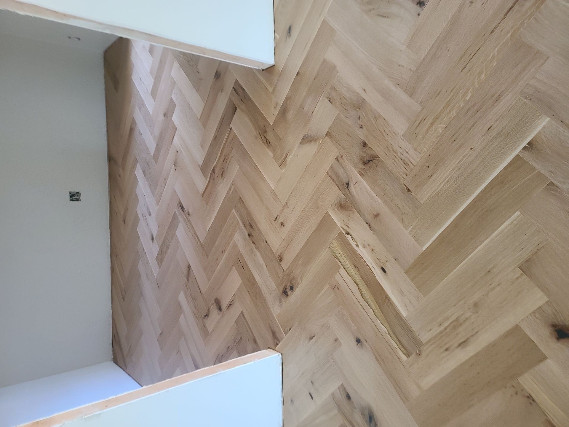 Herringbone wood floor in a room with white walls and a doorway.