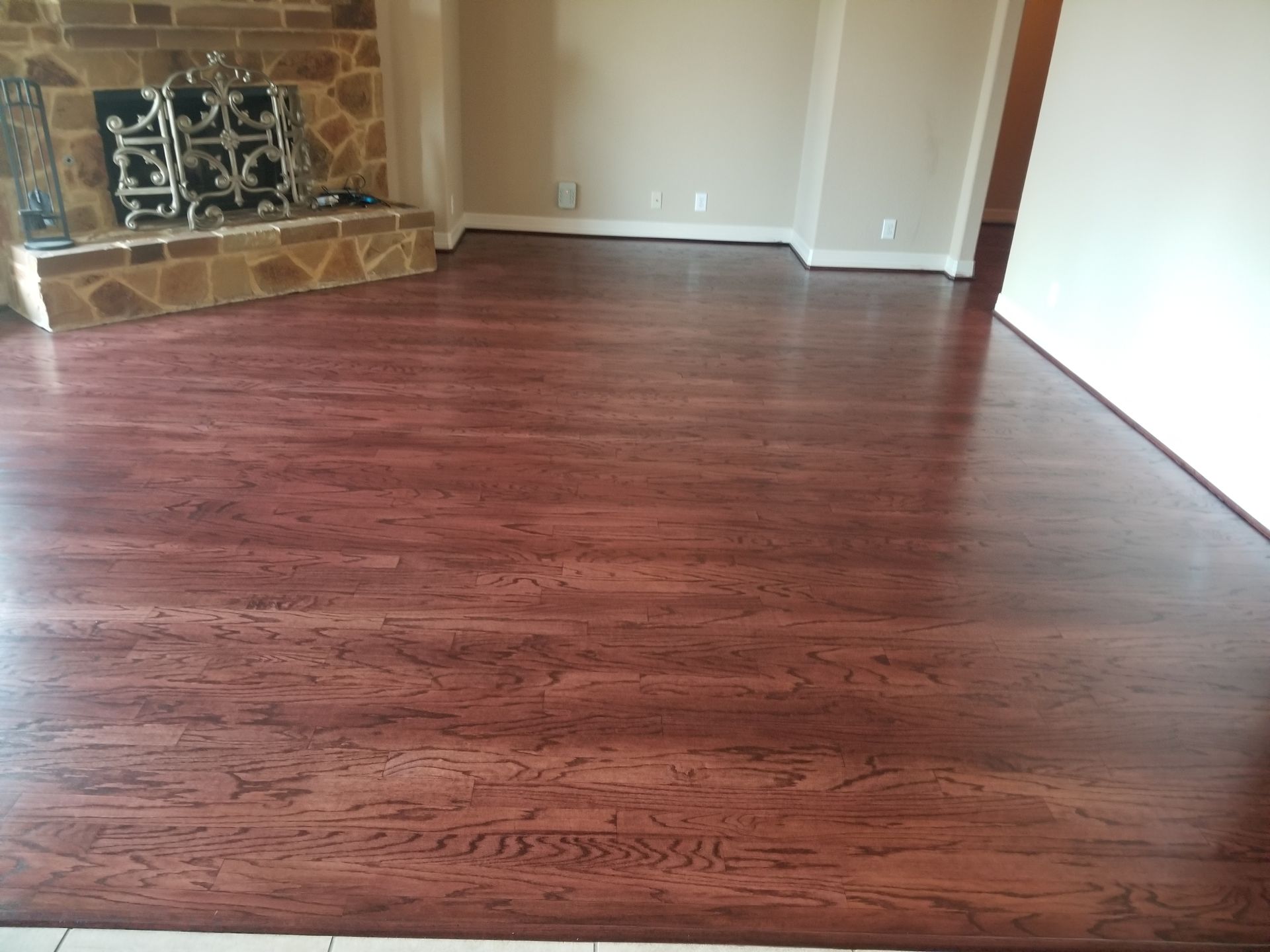 Empty living room with dark hardwood floors and a stone fireplace.