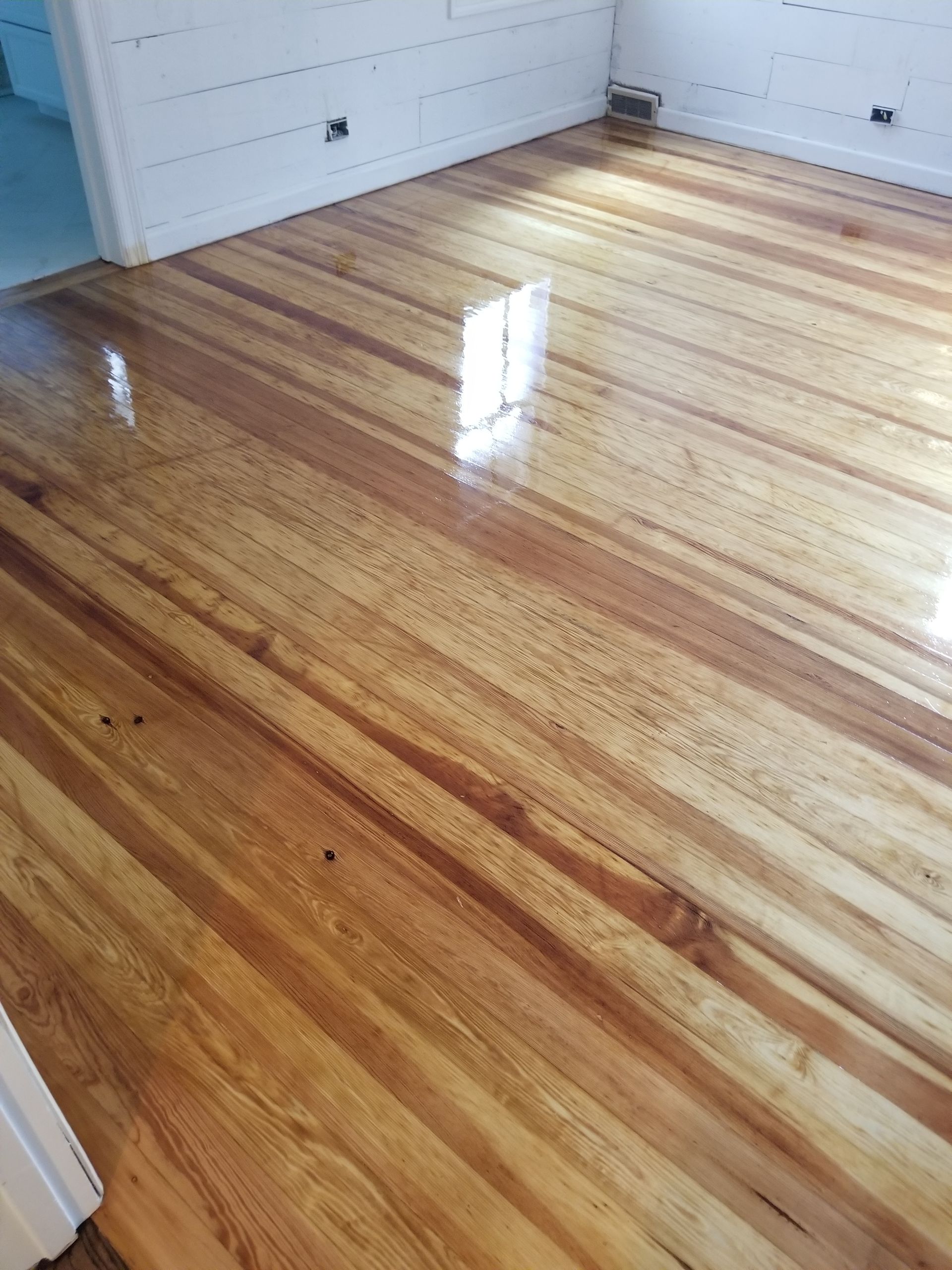 Shiny hardwood floor in an empty room with white walls and sunlight reflection