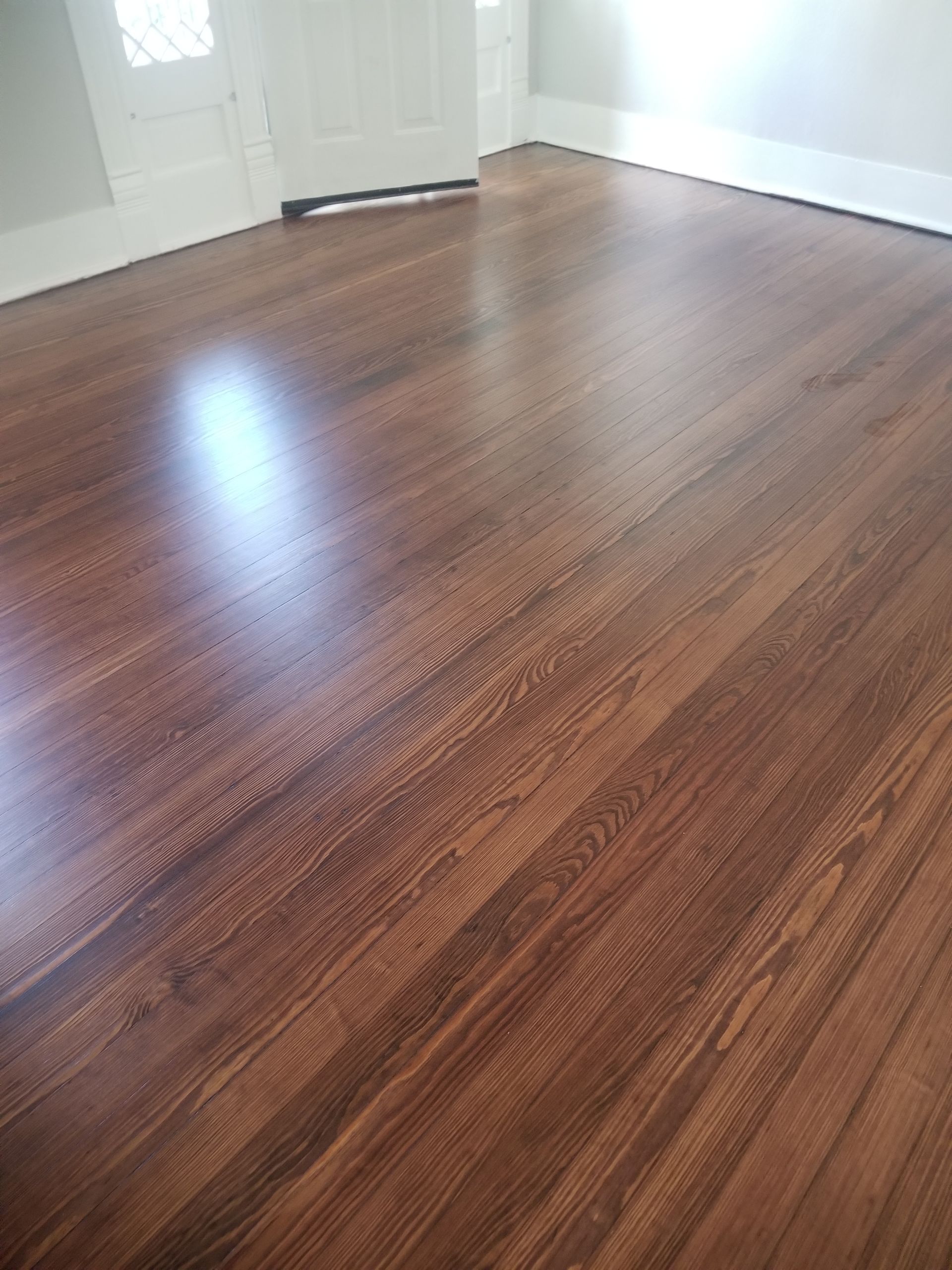 Empty room with glossy dark wood floors and white walls near a doorway.