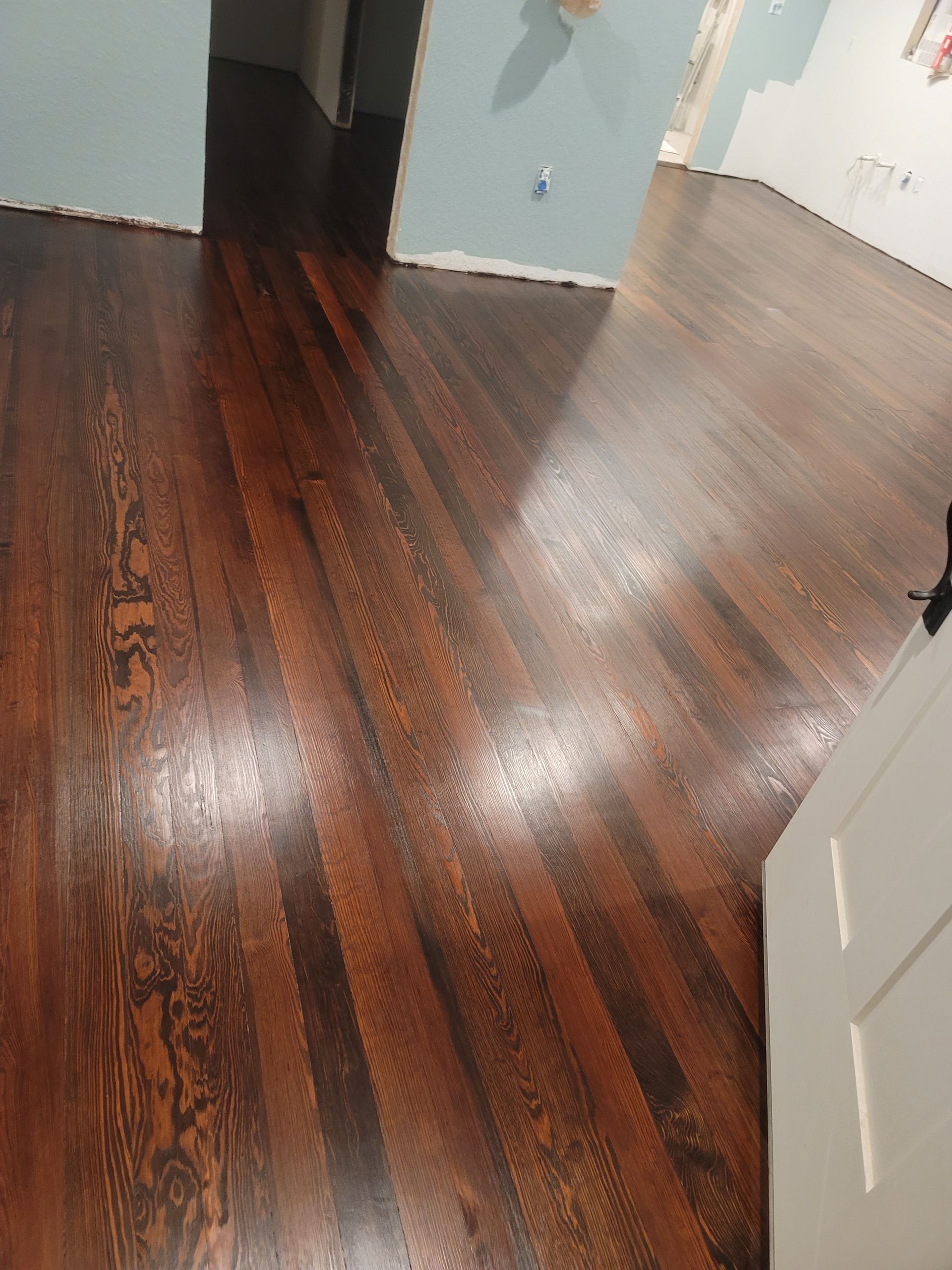 Empty room with glossy dark wood floor and light gray walls, reflecting light.