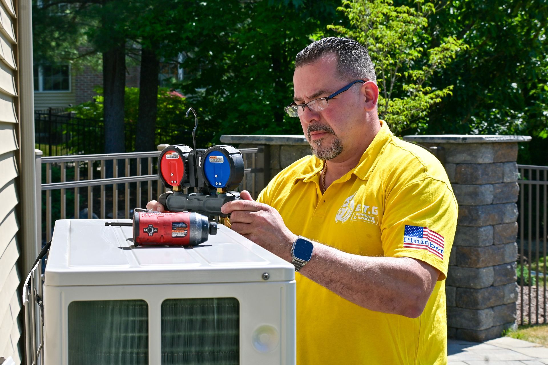 A man in a yellow shirt is working on an air conditioner.