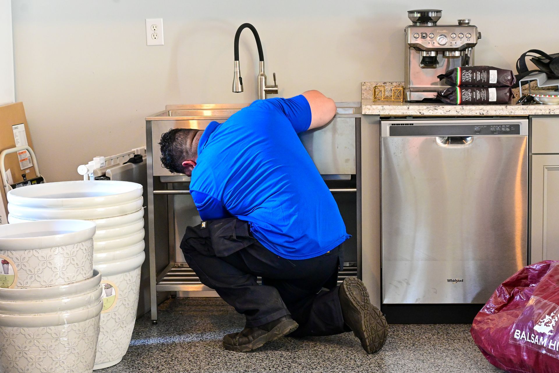 A man in a blue shirt is working on a sink in a kitchen.