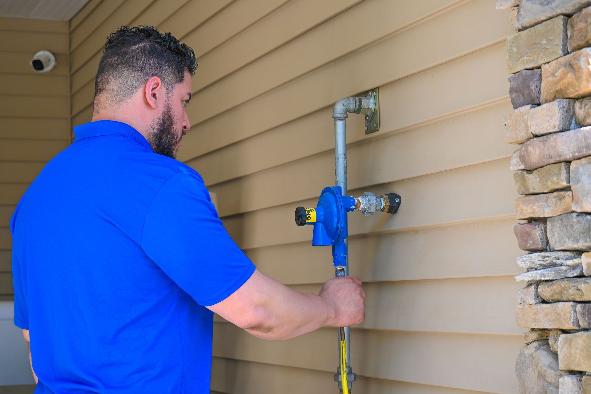 A man in a blue shirt is fixing a faucet on the side of a house.