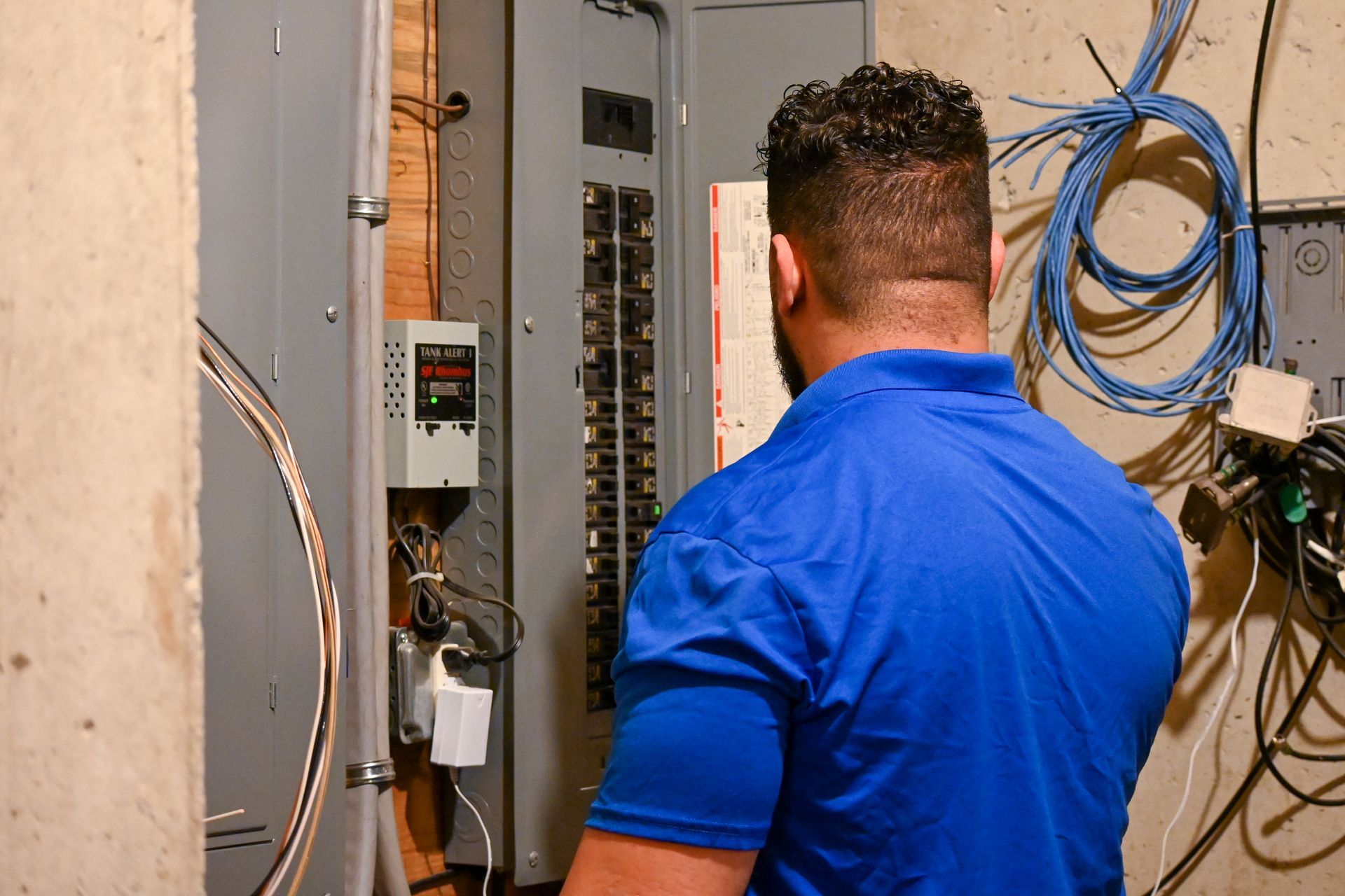 A man in a blue shirt is working on an electrical panel.