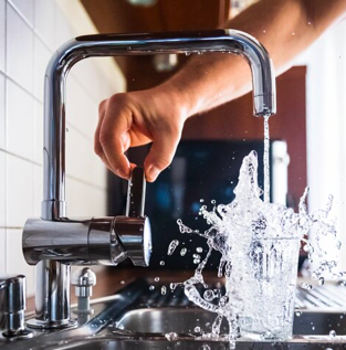 A person is pouring water from a faucet into a glass