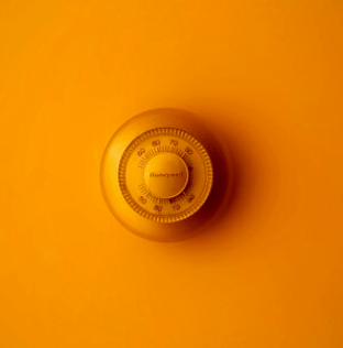 A close up of a yellow thermostat on an orange background.