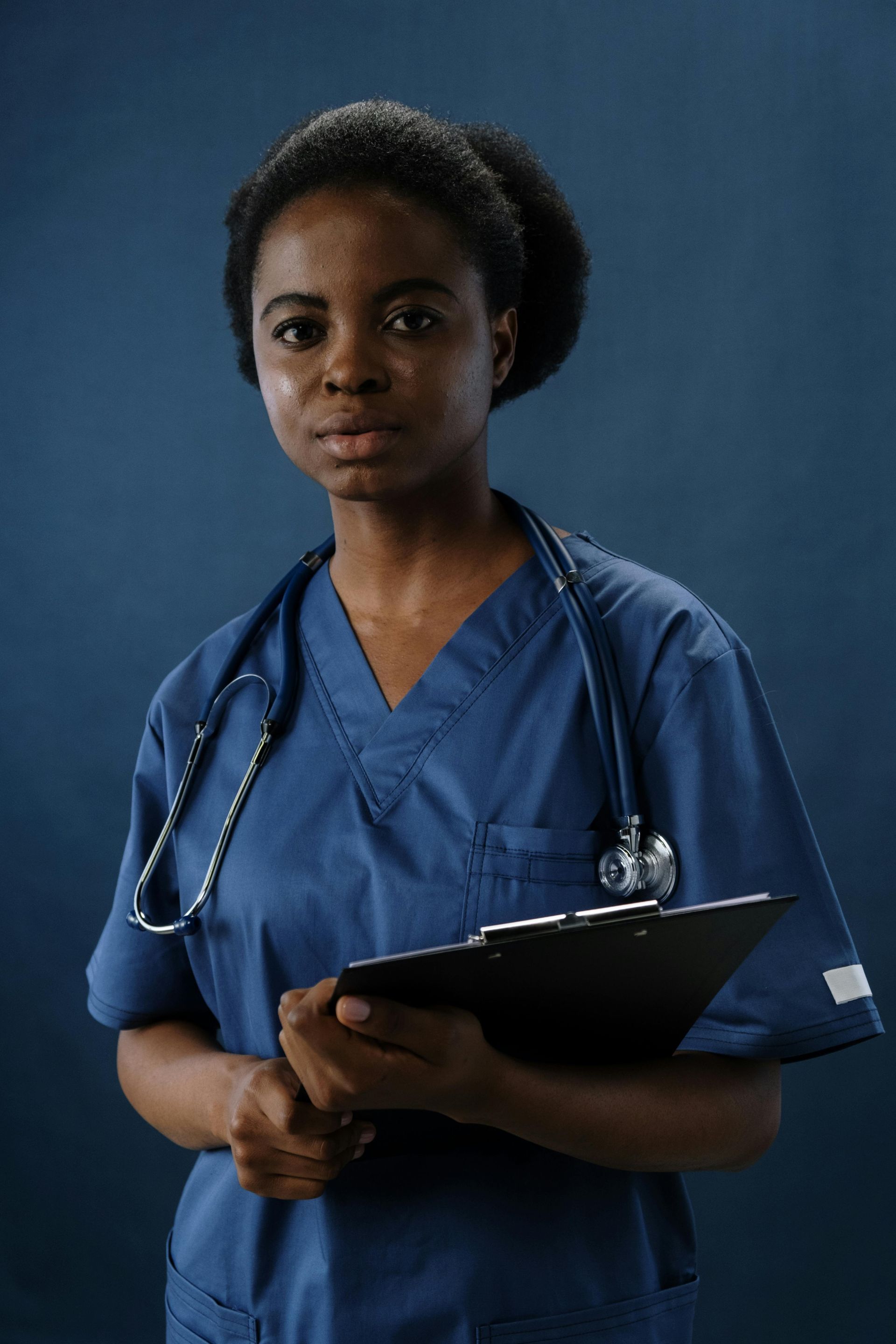 A nurse with a stethoscope around her neck is holding a clipboard.