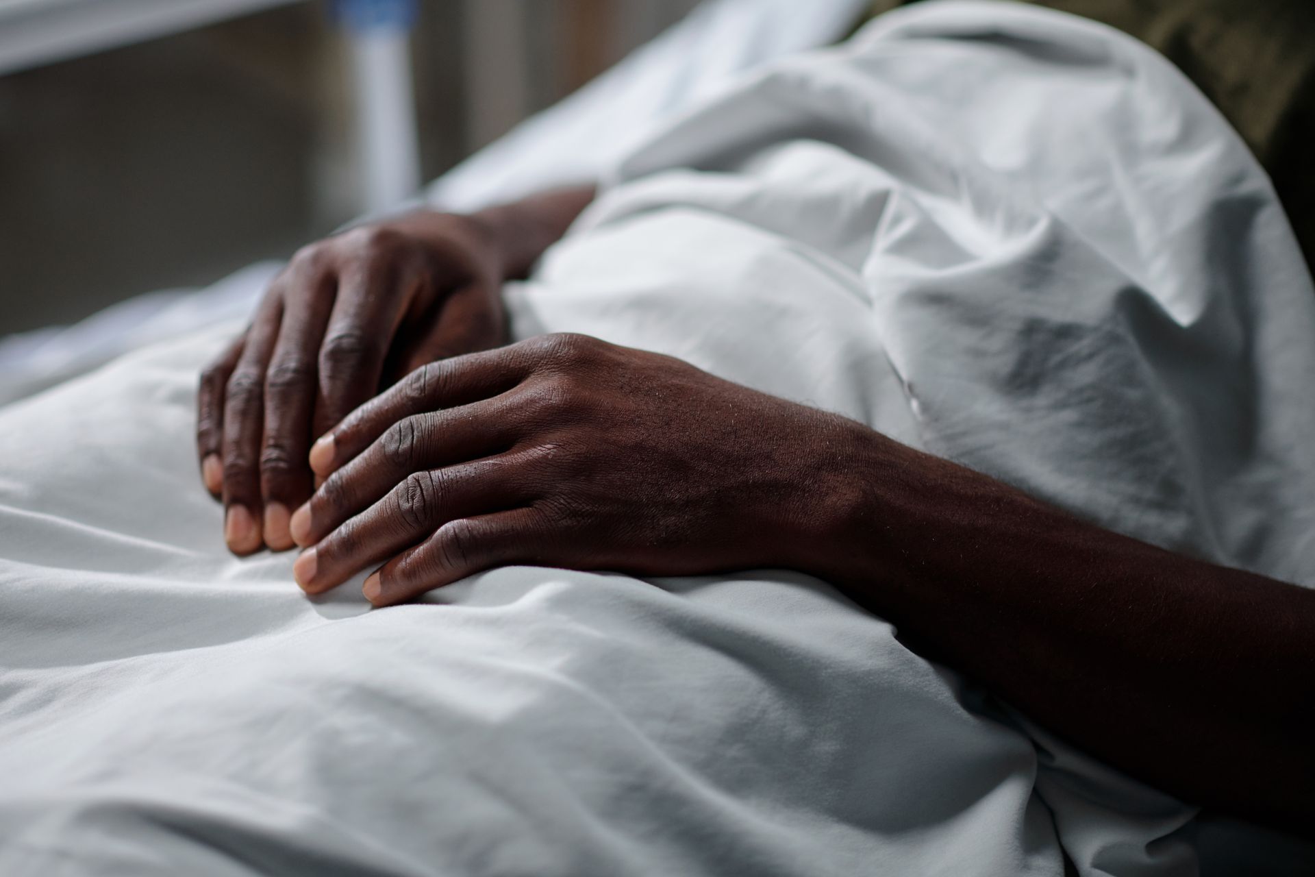 A person is laying in a hospital bed with their hands on the bed.