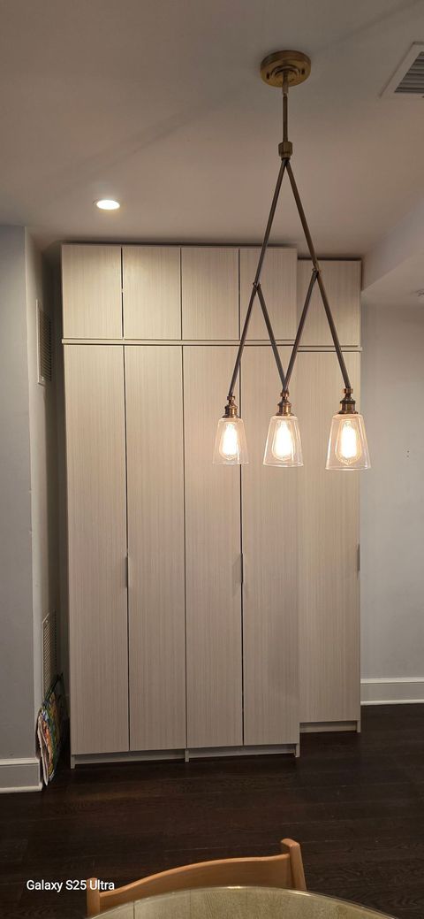 Three-bulb pendant light fixture above wooden cabinets; dark hardwood floor.