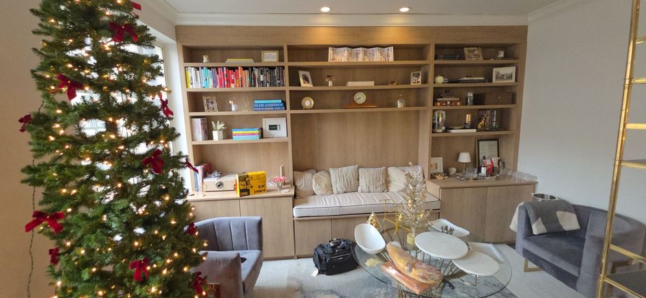 Christmas tree decorated with red bows and lights in front of a built-in bookshelf.