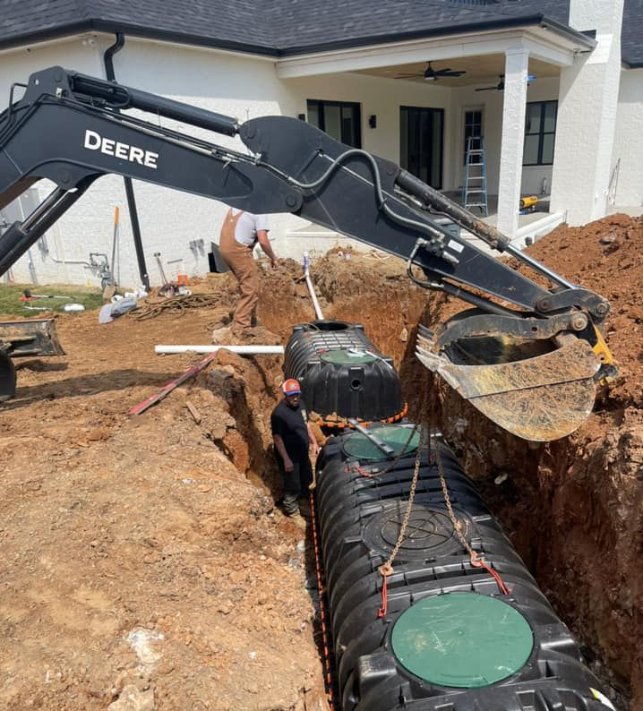 Excavator lifting a septic tank into a trench at a residential construction site.