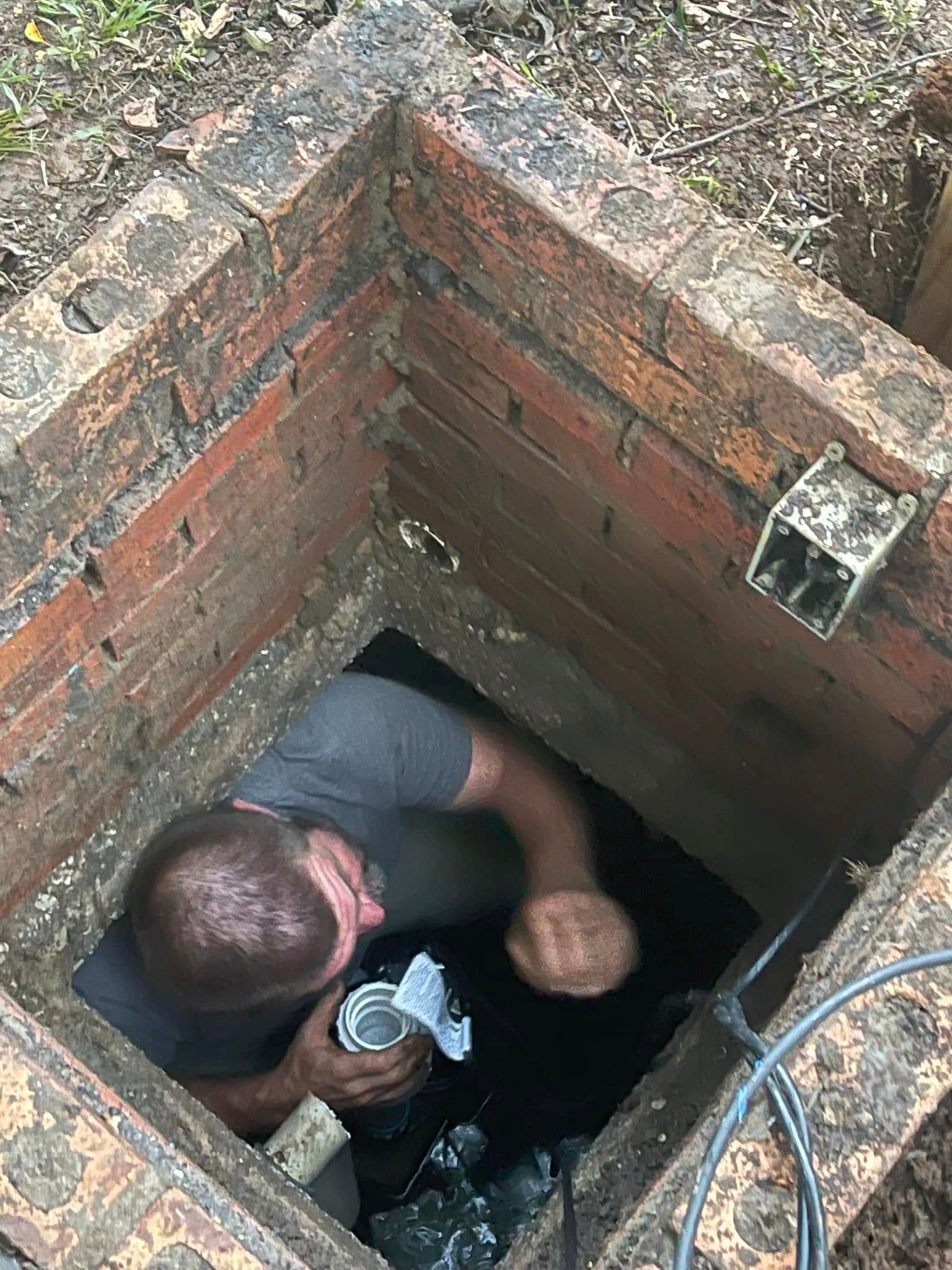 Man inside a brick sewer access point, holding a container, looking down.