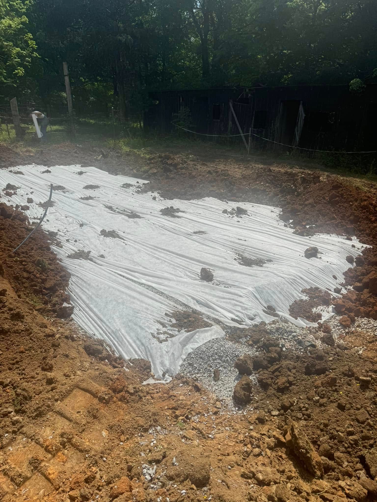 A dug-out area with white fabric laid on the soil, likely for a garden bed or landscaping.
