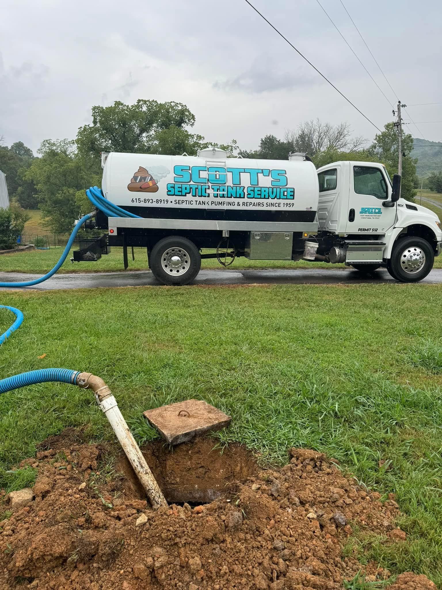 Septic truck servicing a septic tank, with blue hose connected to tank opening.