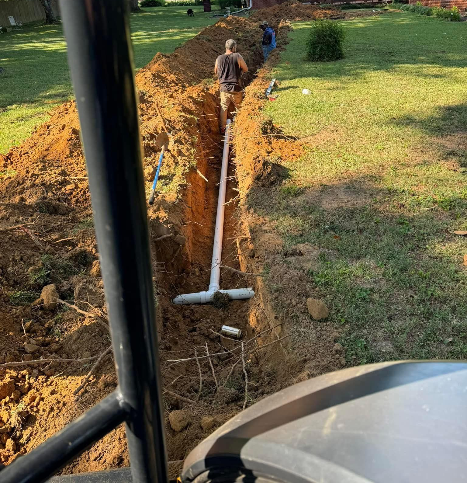 Workers installing PVC pipes in a trench in a grassy yard.
