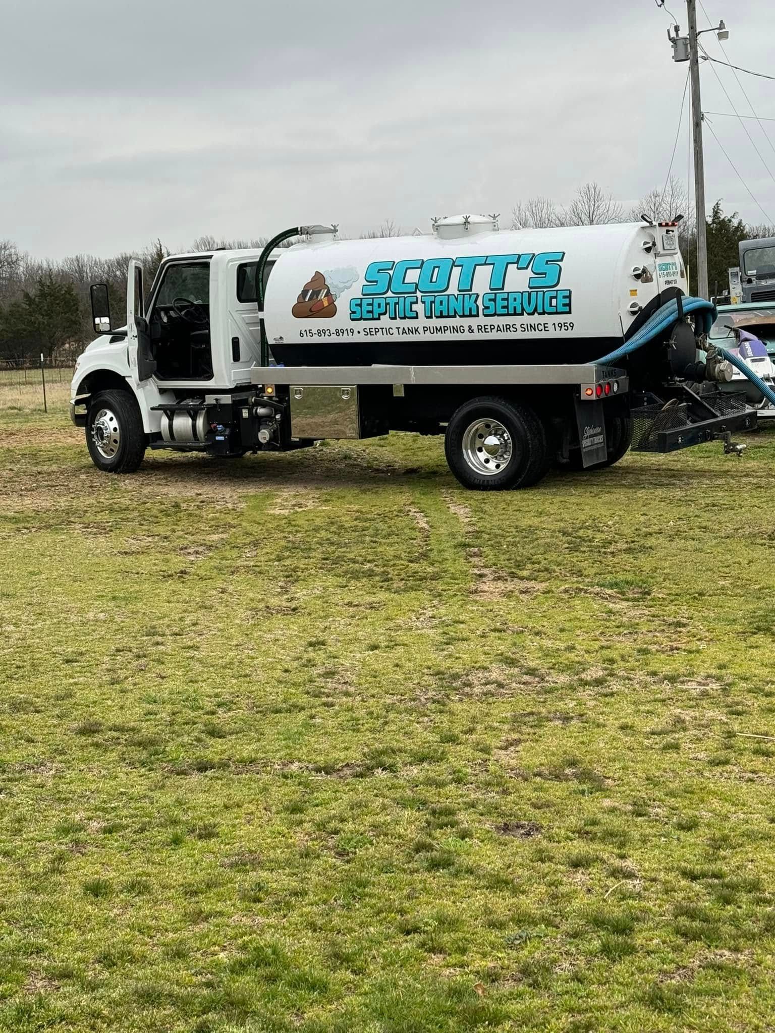 White septic service truck with blue text, parked on grass.