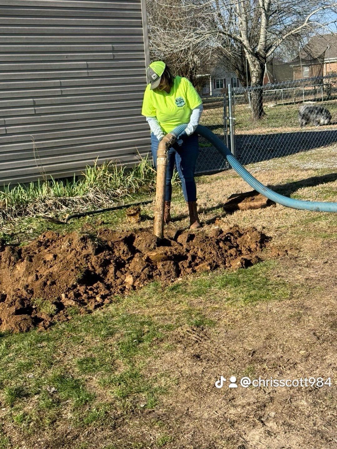 Person in neon shirt using tool on soil next to building.