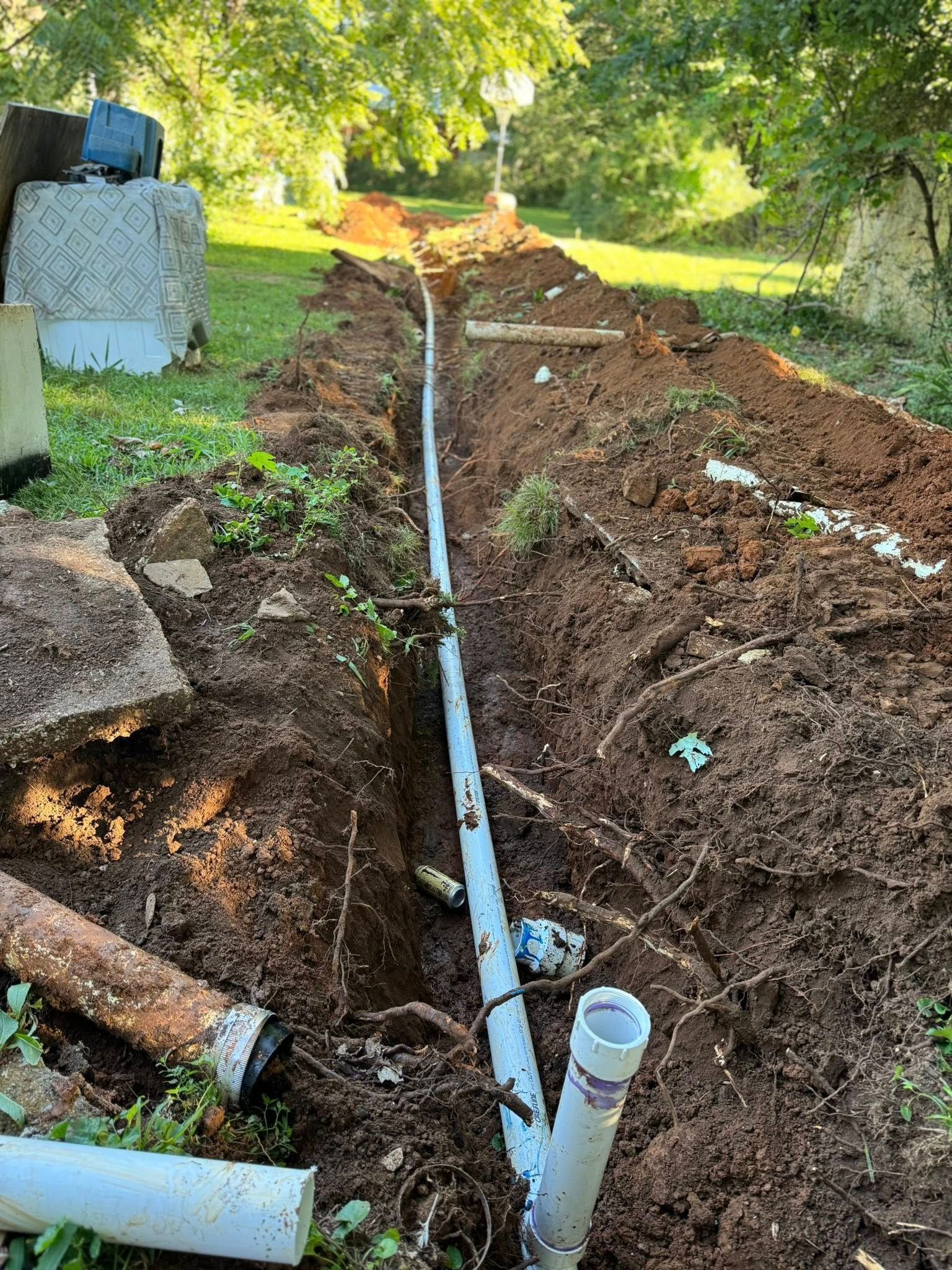 A trench dug for piping. A long, straight trench contains gray PVC pipes in a grassy outdoor setting.