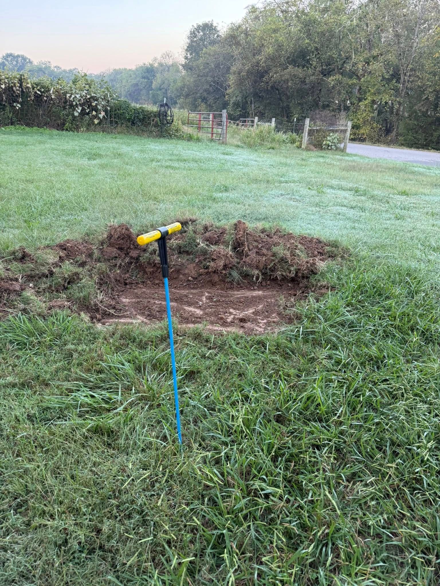 Dirt patch in grass with garden tool, walkway and trees in background.