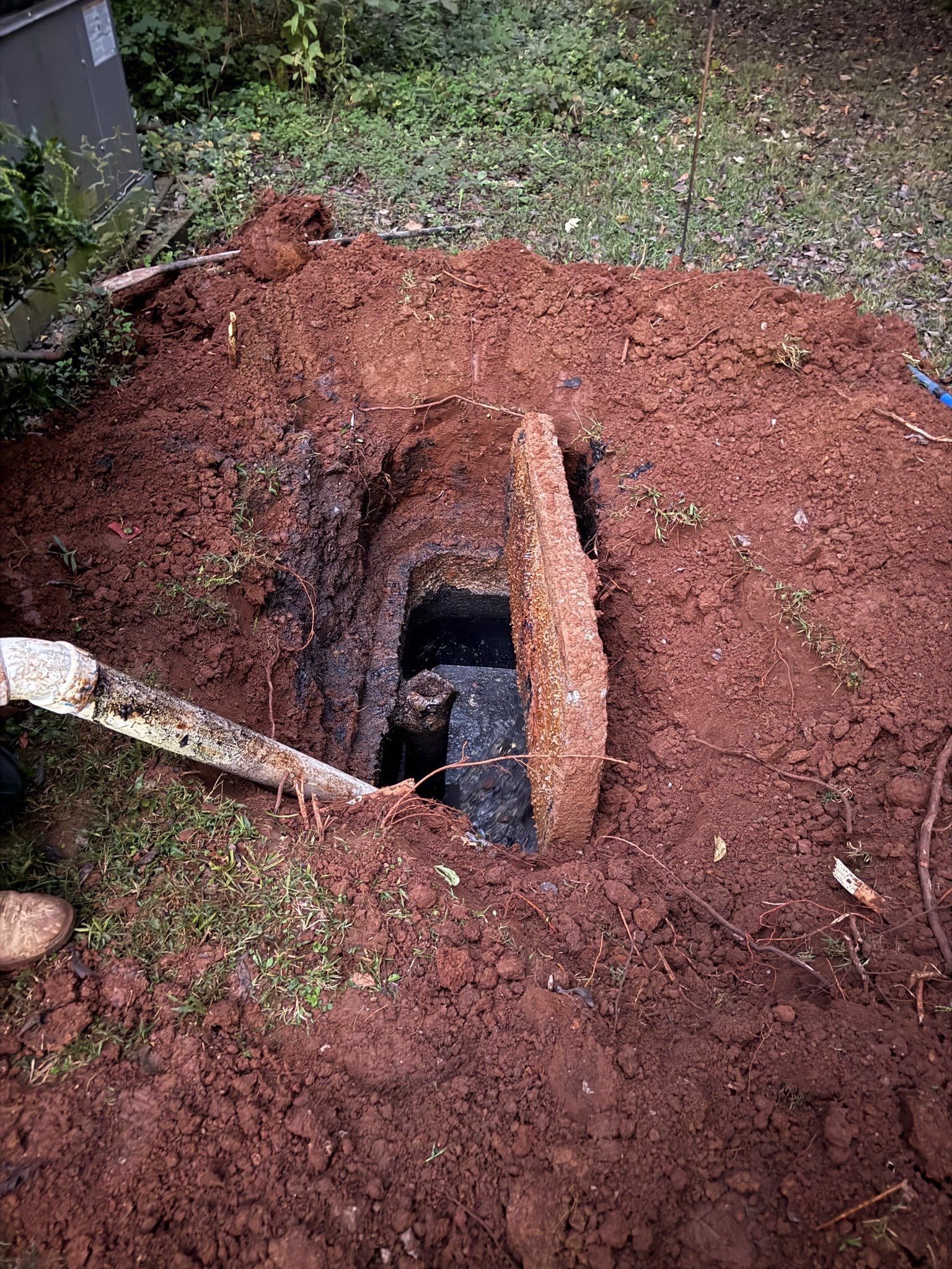 A rectangular hole in the ground with an open, dark chamber, surrounded by reddish-brown soil.