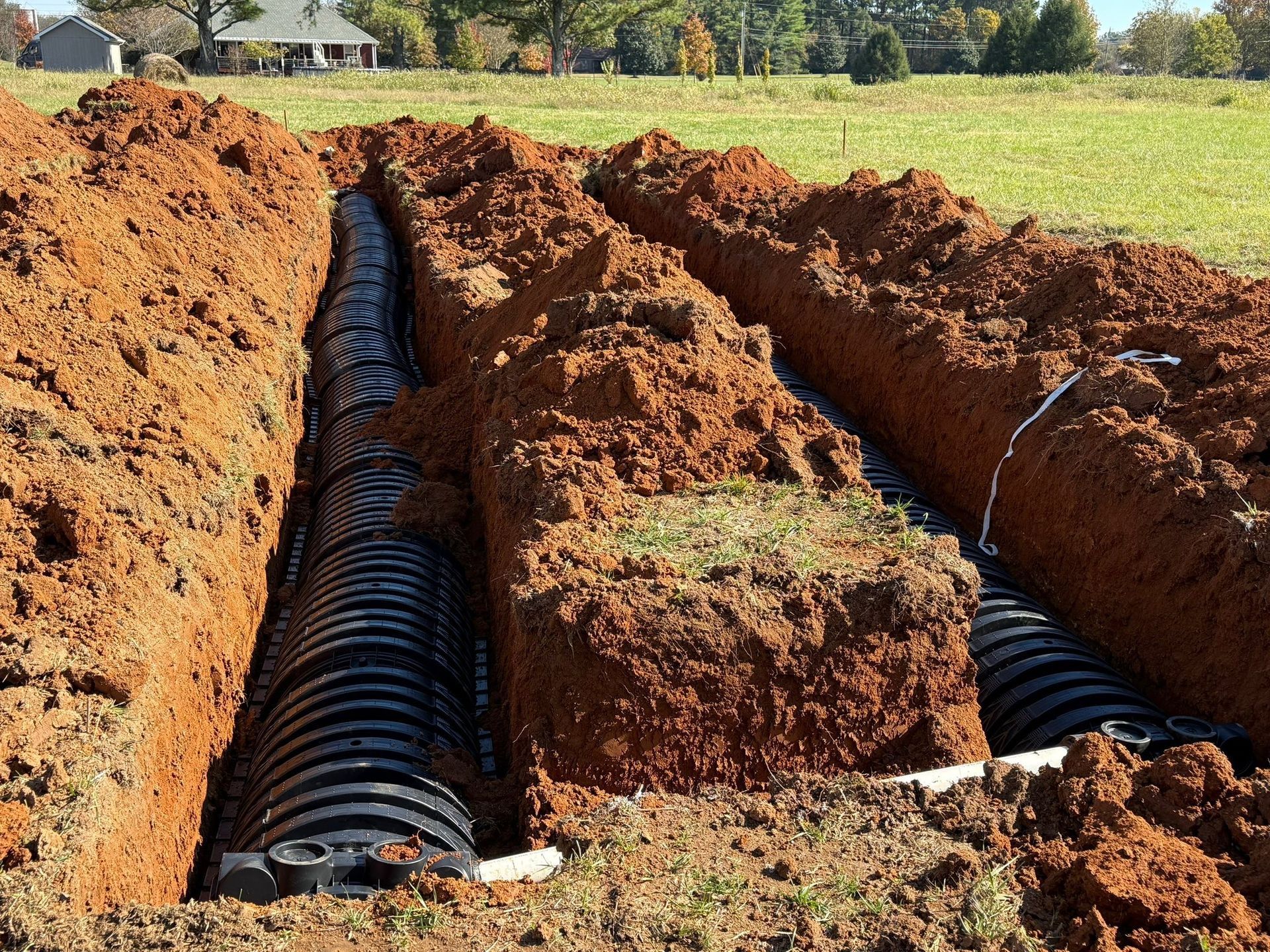 Trenches with black plastic drain pipes in a grassy field. Construction site.