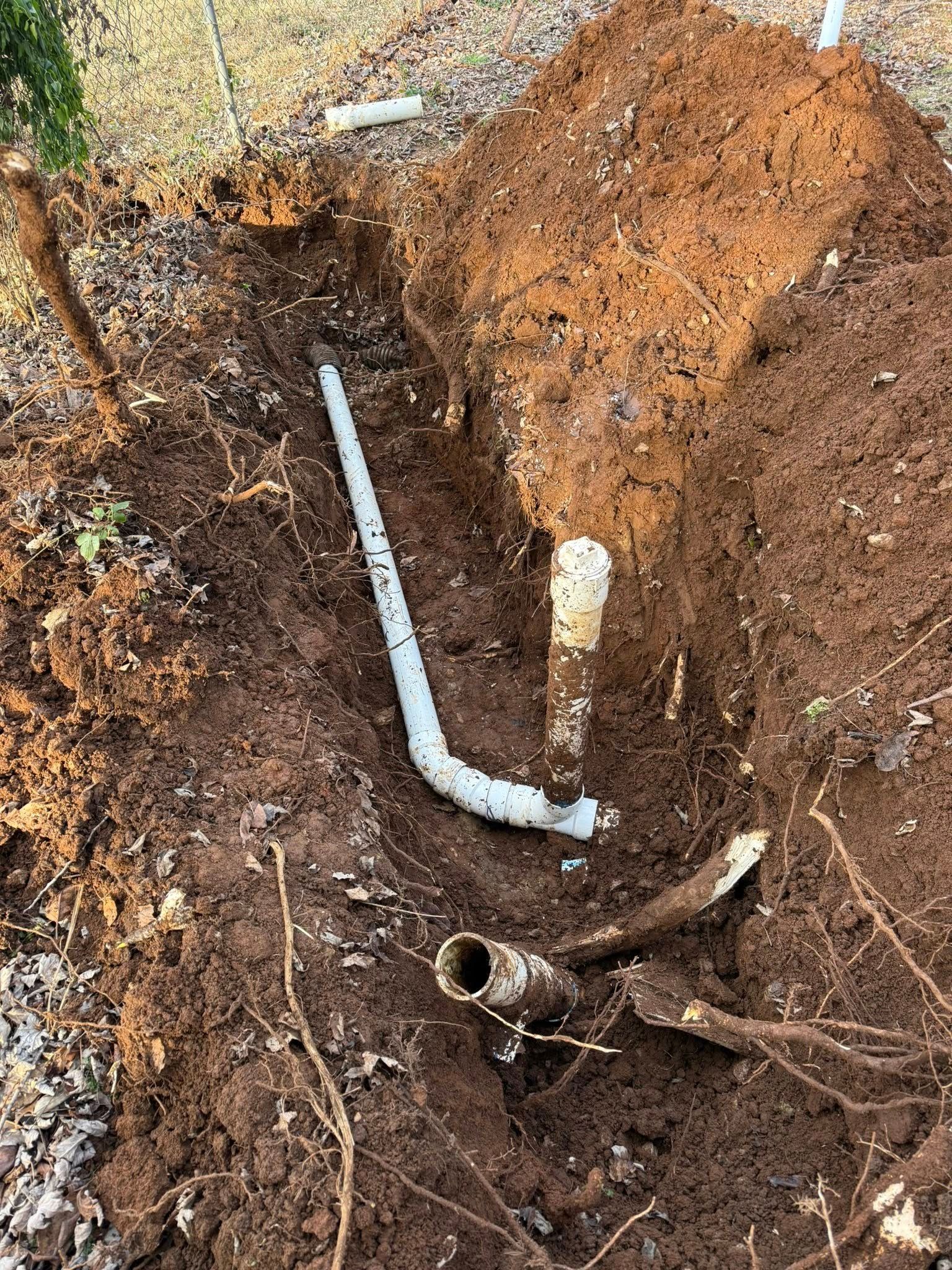 Trench with exposed PVC pipes and brown soil. One pipe is broken.