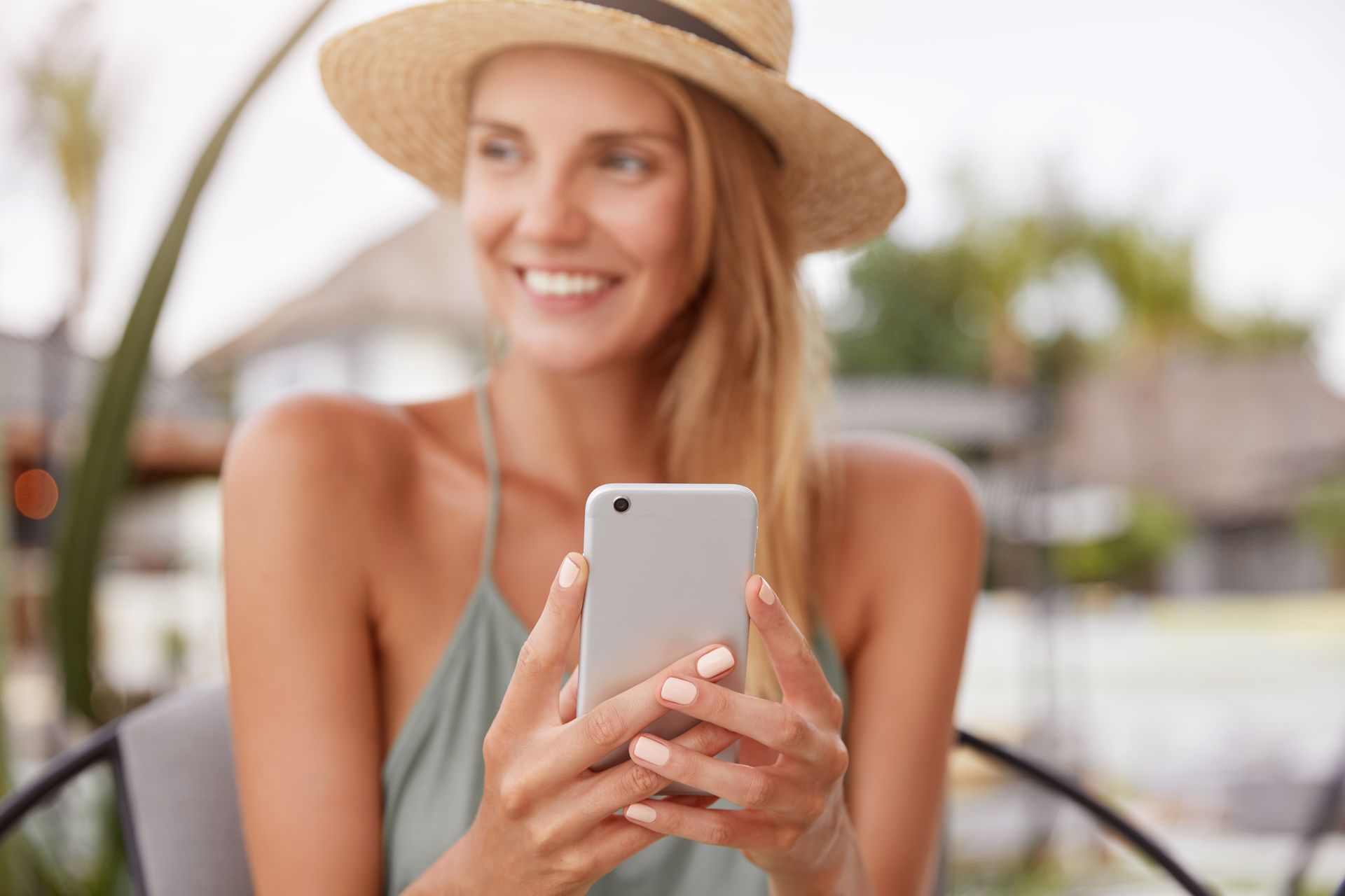 A woman wearing a straw hat is holding a cell phone in her hands.