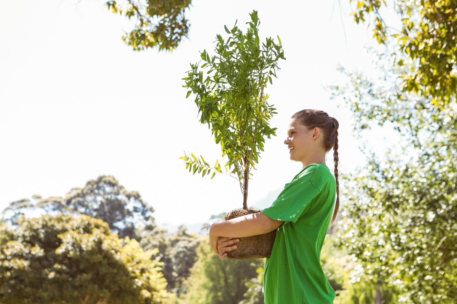 A woman in a green shirt is holding a small tree in a basket.