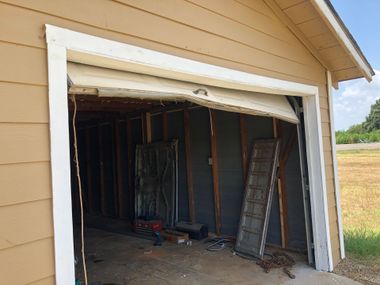 Partially damaged garage opening with bent white trim and exposed interior framing