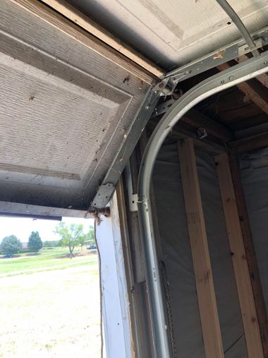 Open garage door corner with metal tracks, insulation, and daylight outside