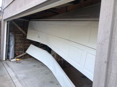 Collapsed garage door bent inward after a structural failure, with debris and exposed framing.